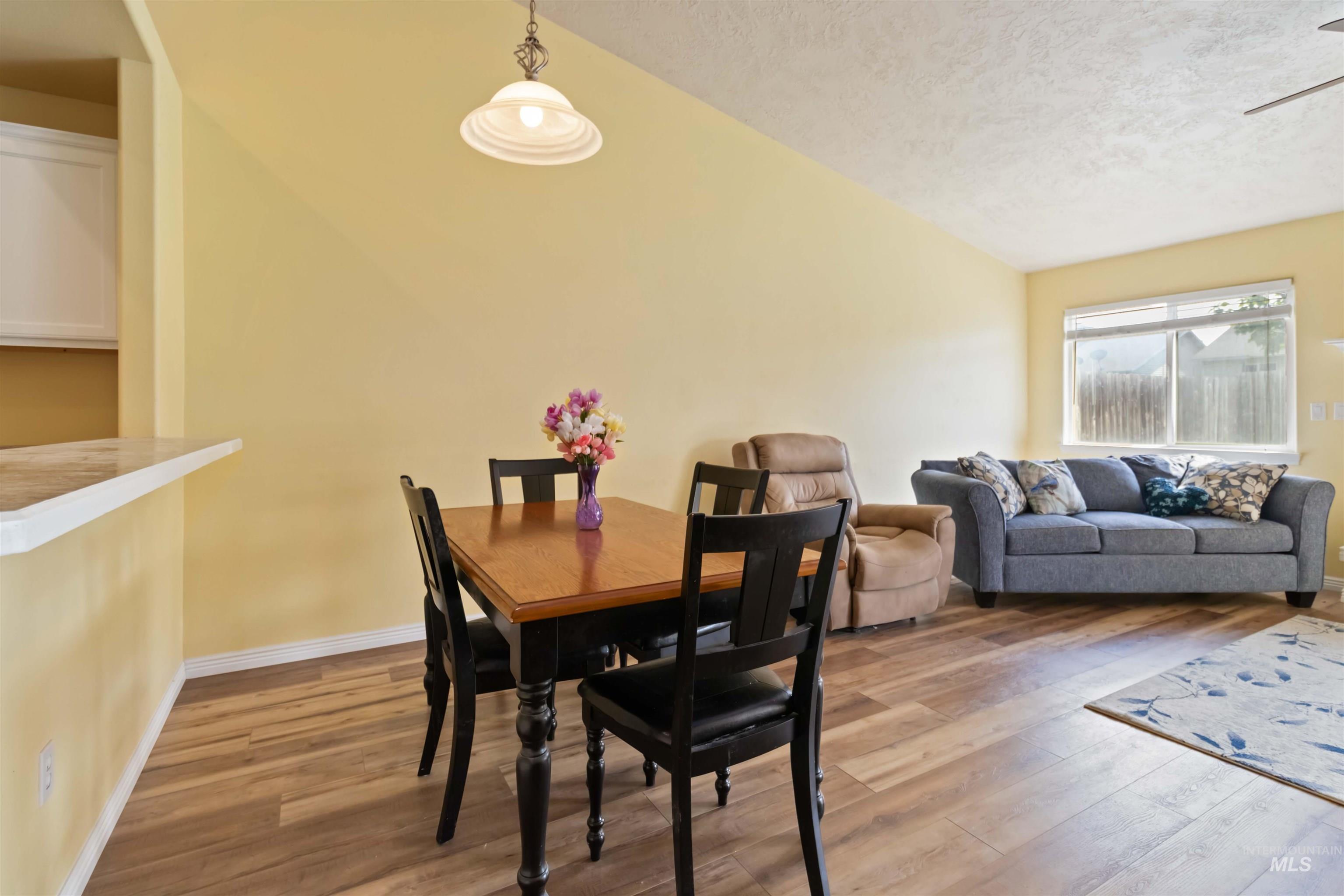 Dining room with light wood-type flooring, a textured ceiling, vaulted ceiling, and ceiling fan