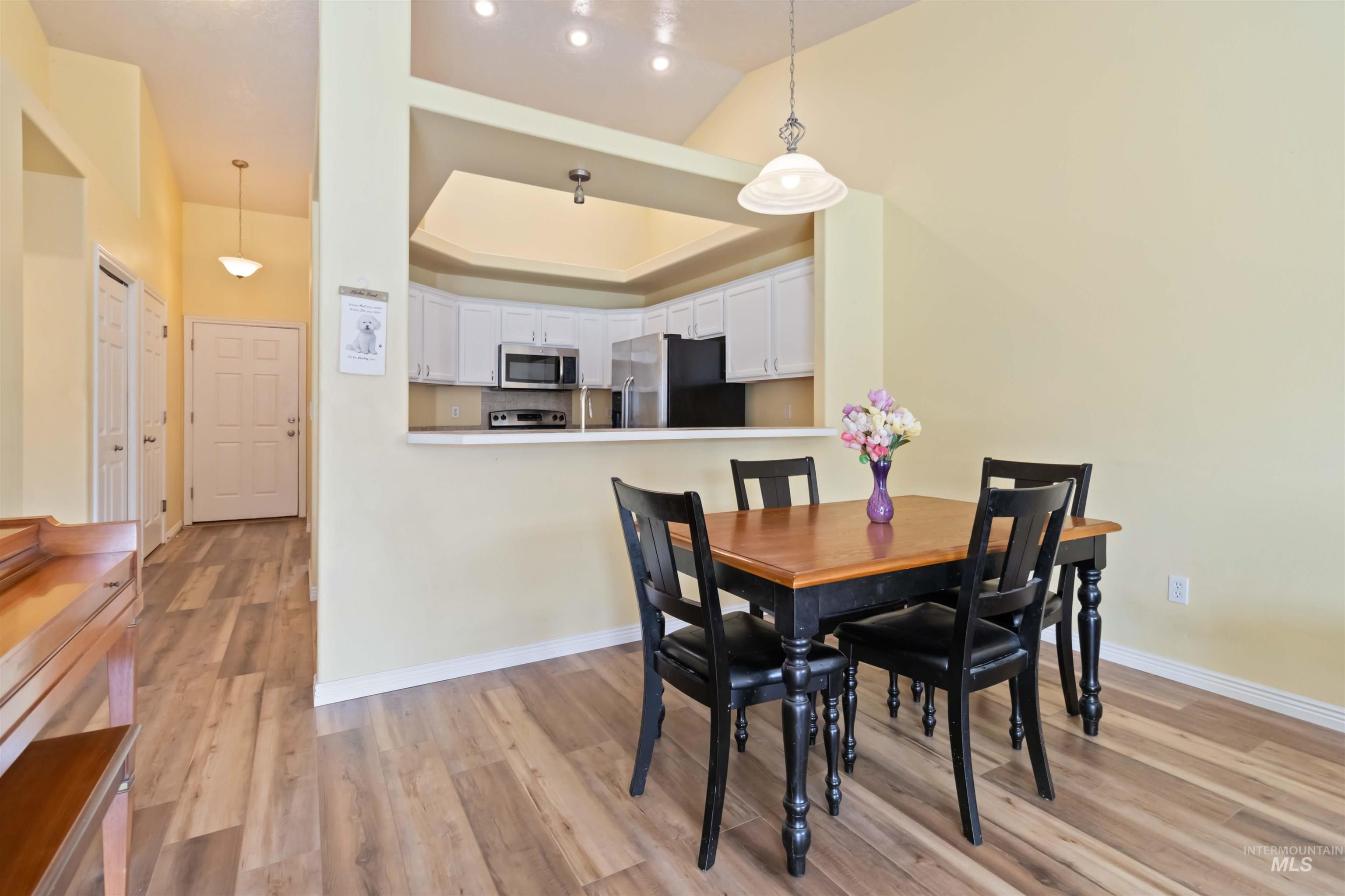 Dining space with light wood-type flooring, a tray ceiling, and vaulted ceiling