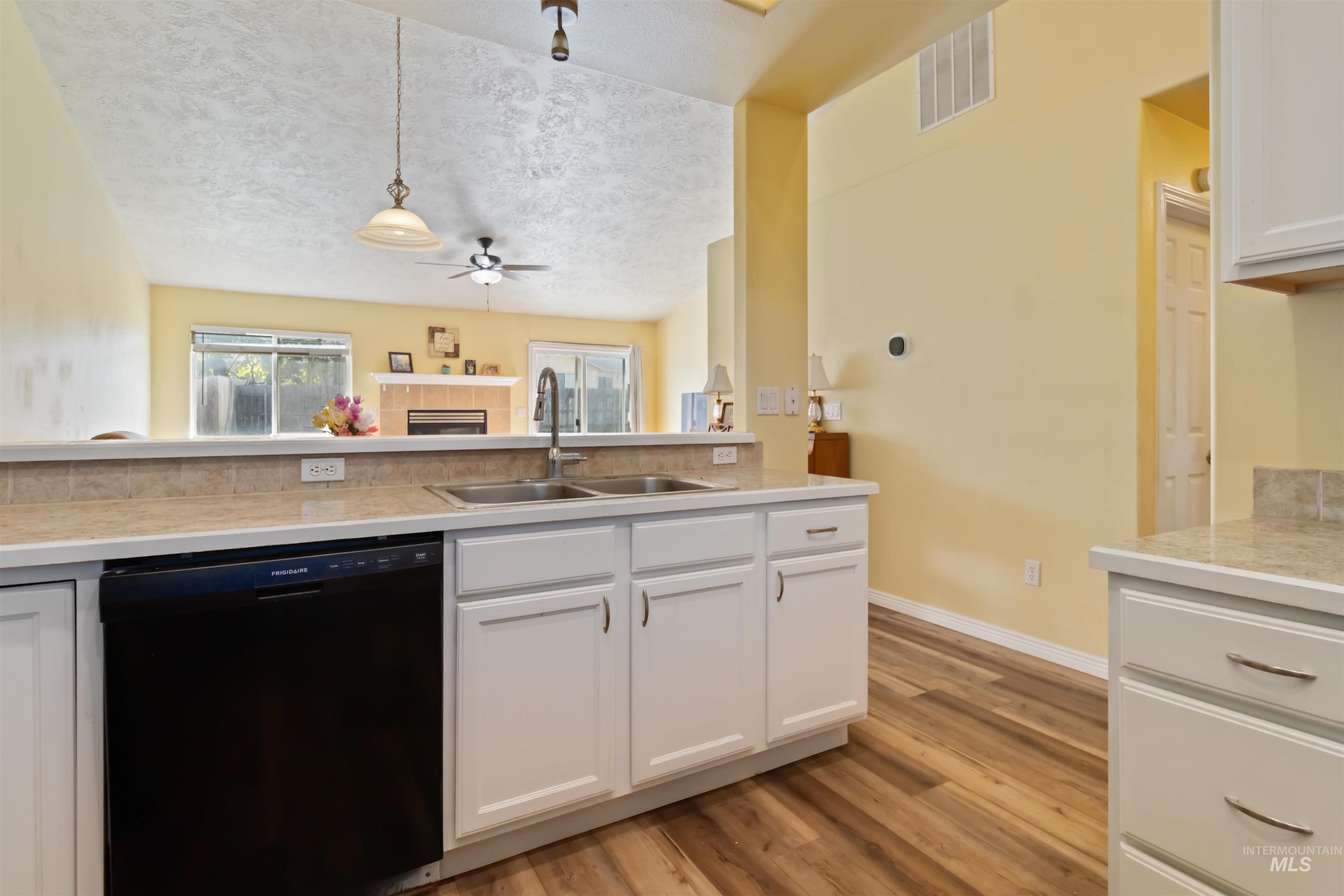Kitchen with white cabinetry, dishwasher, pendant lighting, light wood-type flooring, and a textured ceiling