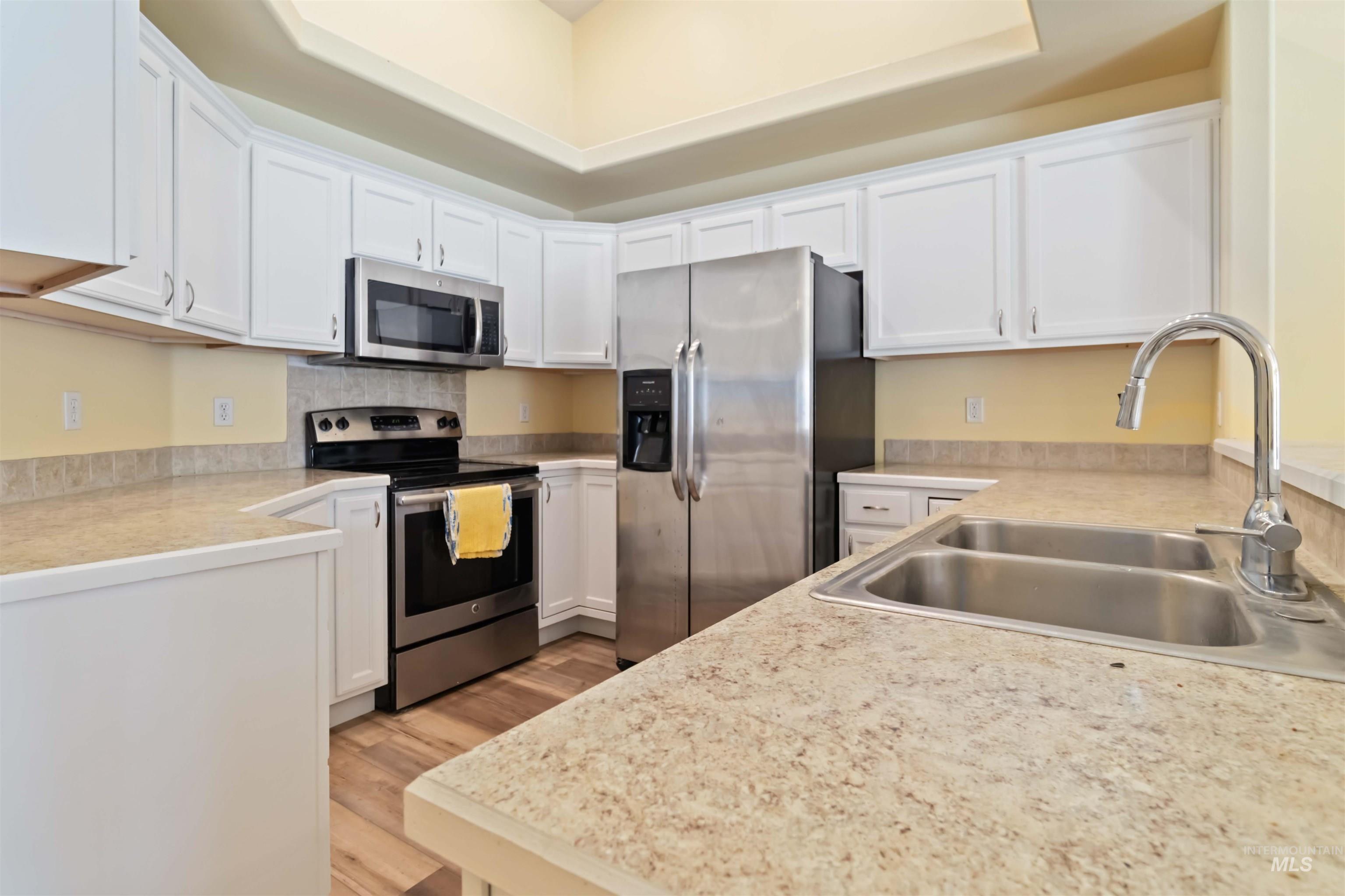 Kitchen featuring light countertops, appliances with stainless steel finishes, white cabinetry, and light wood-style floors