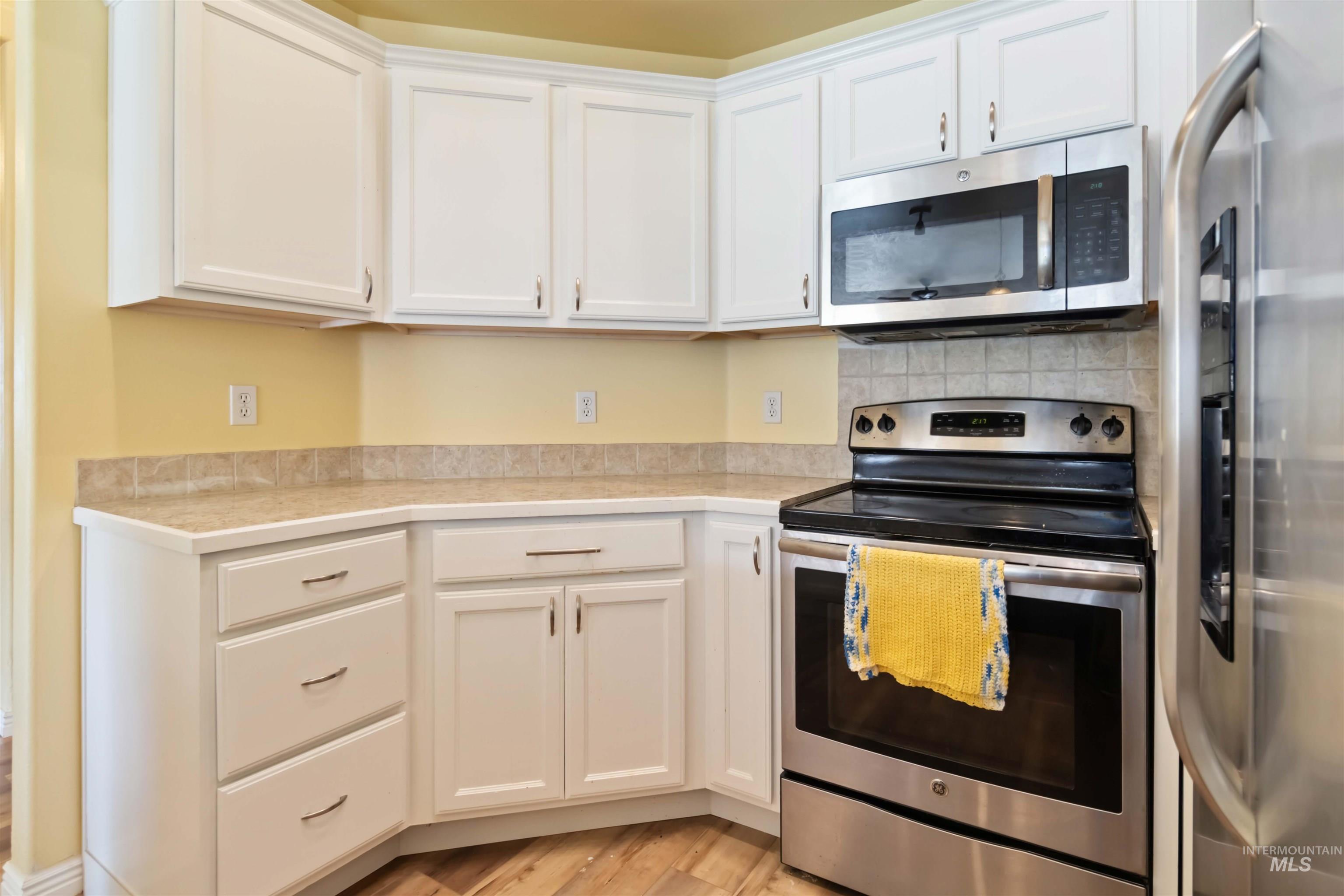 Kitchen with appliances with stainless steel finishes, white cabinets, light countertops, and light wood finished floors