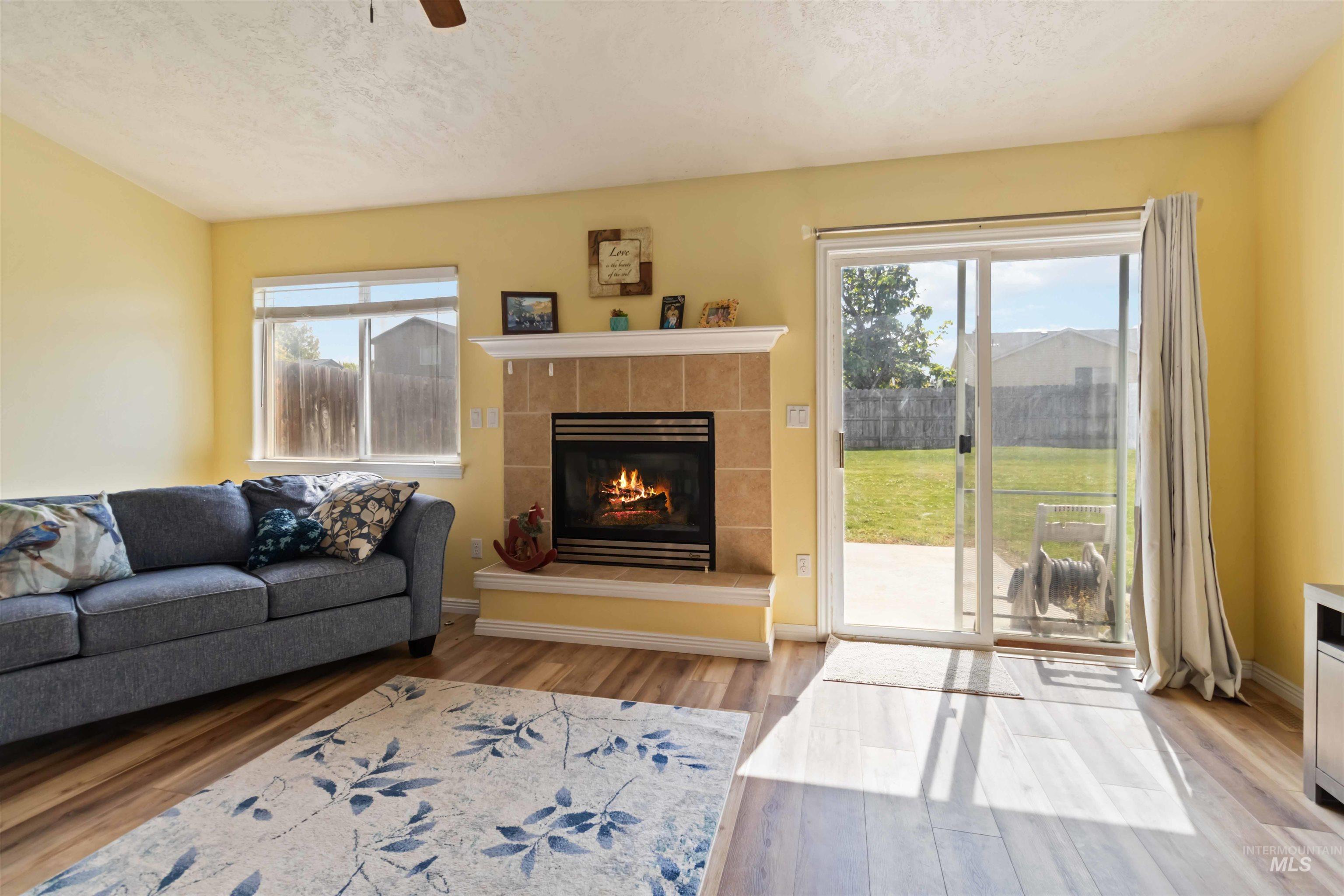 Living area featuring light wood finished floors, a textured ceiling, a fireplace, and ceiling fan