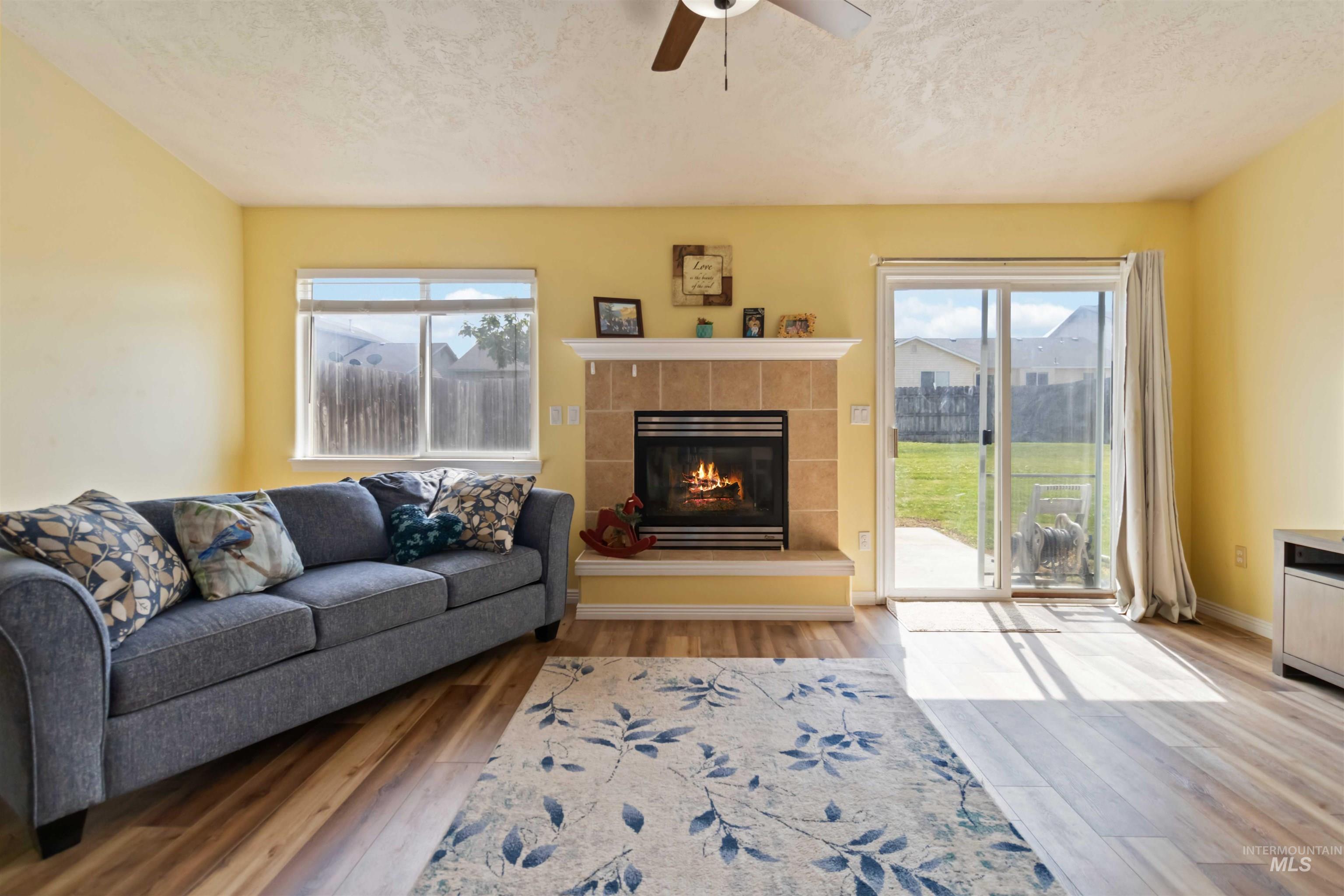 Living area with a fireplace, a textured ceiling, light wood finished floors, and ceiling fan
