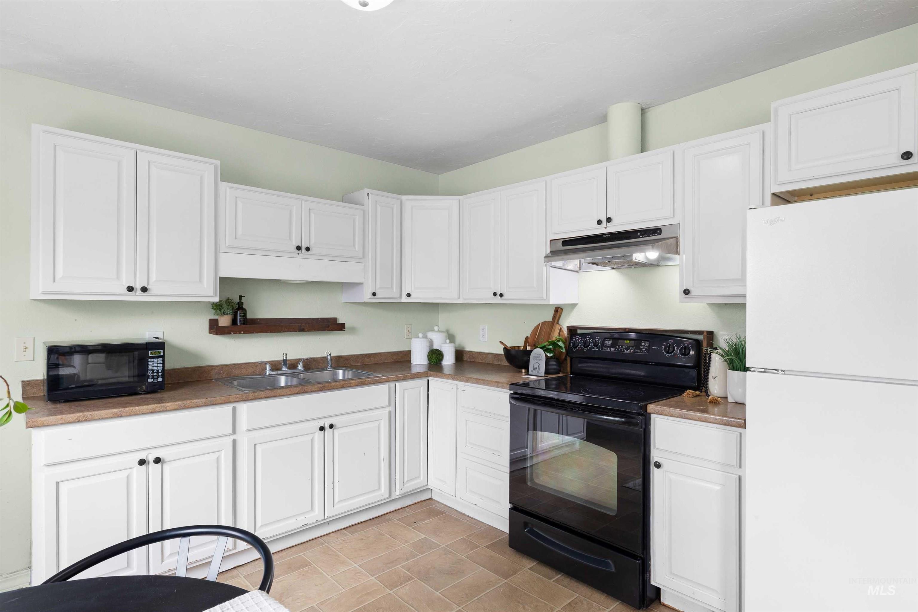 Kitchen featuring black appliances, white cabinetry, under cabinet range hood, and dark countertops