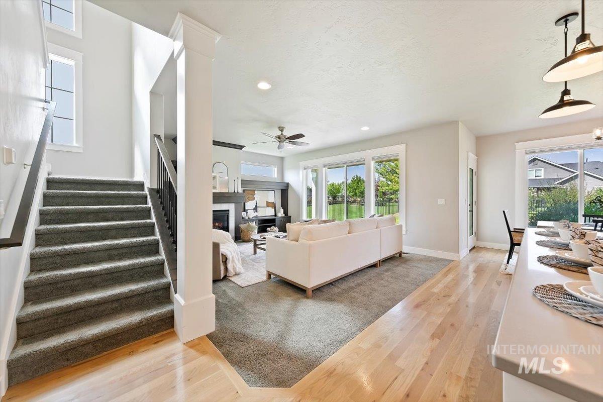 Living room featuring recessed lighting, light wood finished floors, a warm lit fireplace, a ceiling fan, and stairs