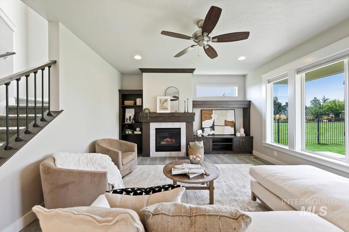 Living room featuring a fireplace, ceiling fan, stairs, recessed lighting, and wood finished floors