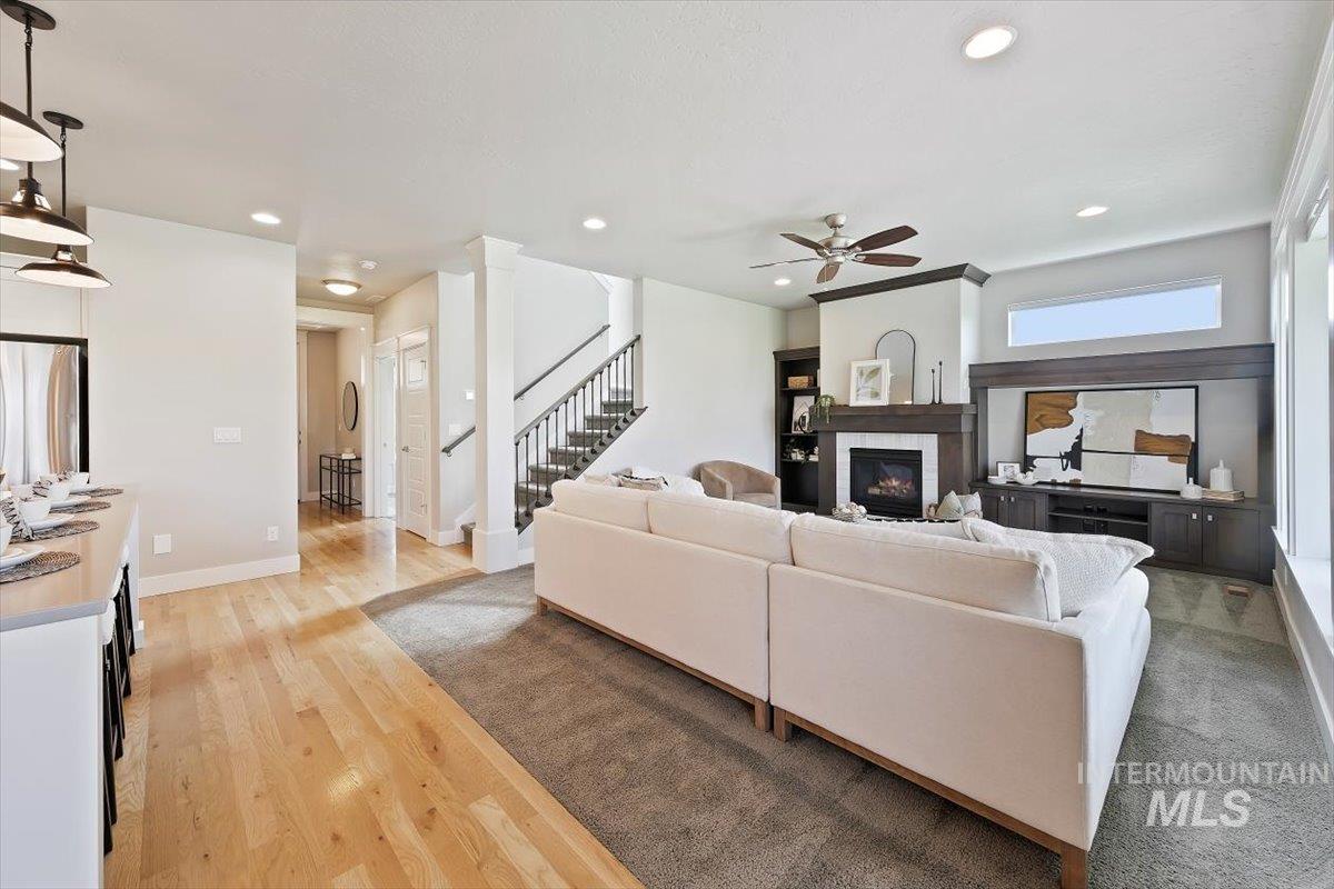 Living area with light wood-style flooring, recessed lighting, a glass covered fireplace, stairway, and a ceiling fan