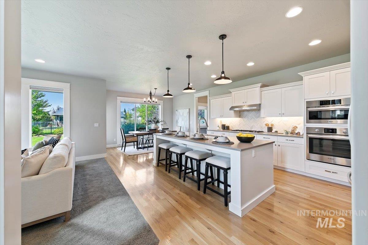 Kitchen with a kitchen breakfast bar, backsplash, hanging light fixtures, white cabinets, and an island with sink