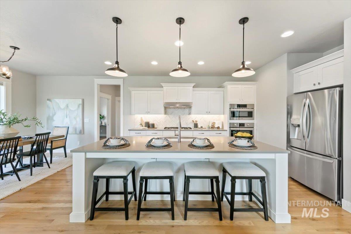 Kitchen with stainless steel appliances, white cabinets, decorative backsplash, a breakfast bar area, and light wood finished floors