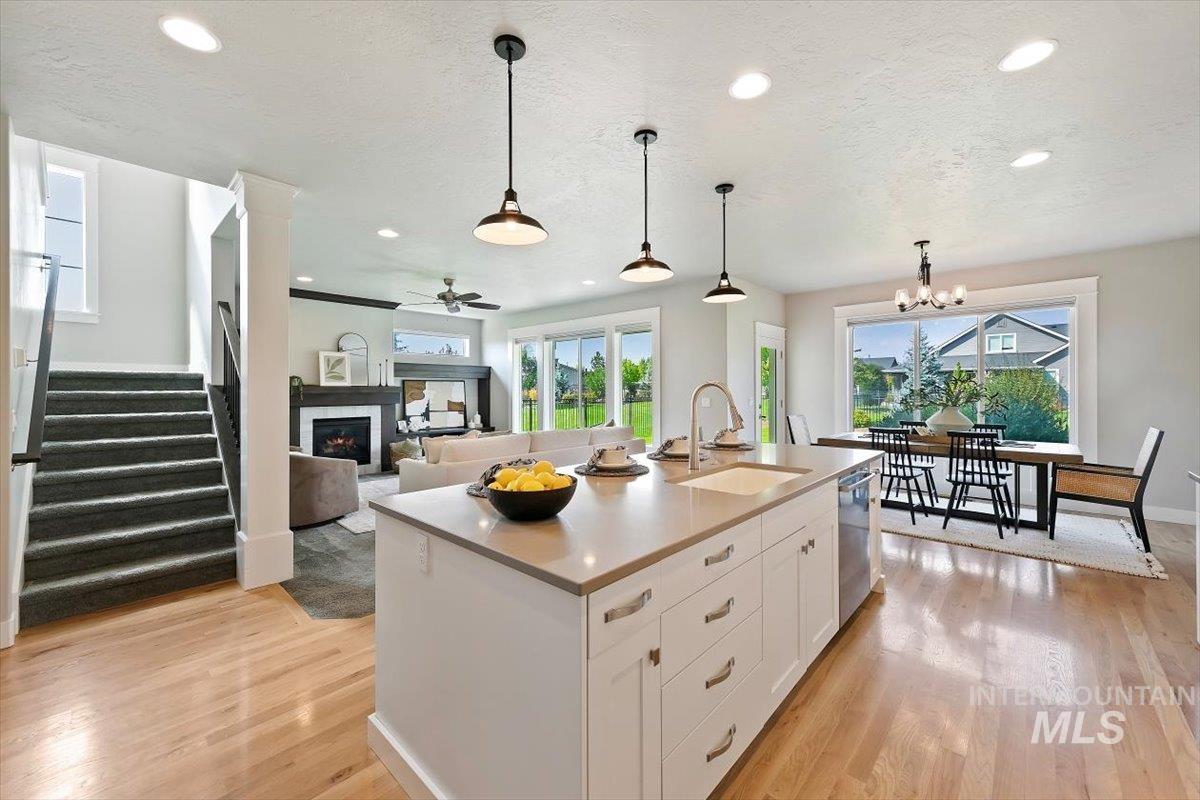 Kitchen featuring white cabinetry, a warm lit fireplace, hanging light fixtures, light wood-style flooring, and healthy amount of natural light