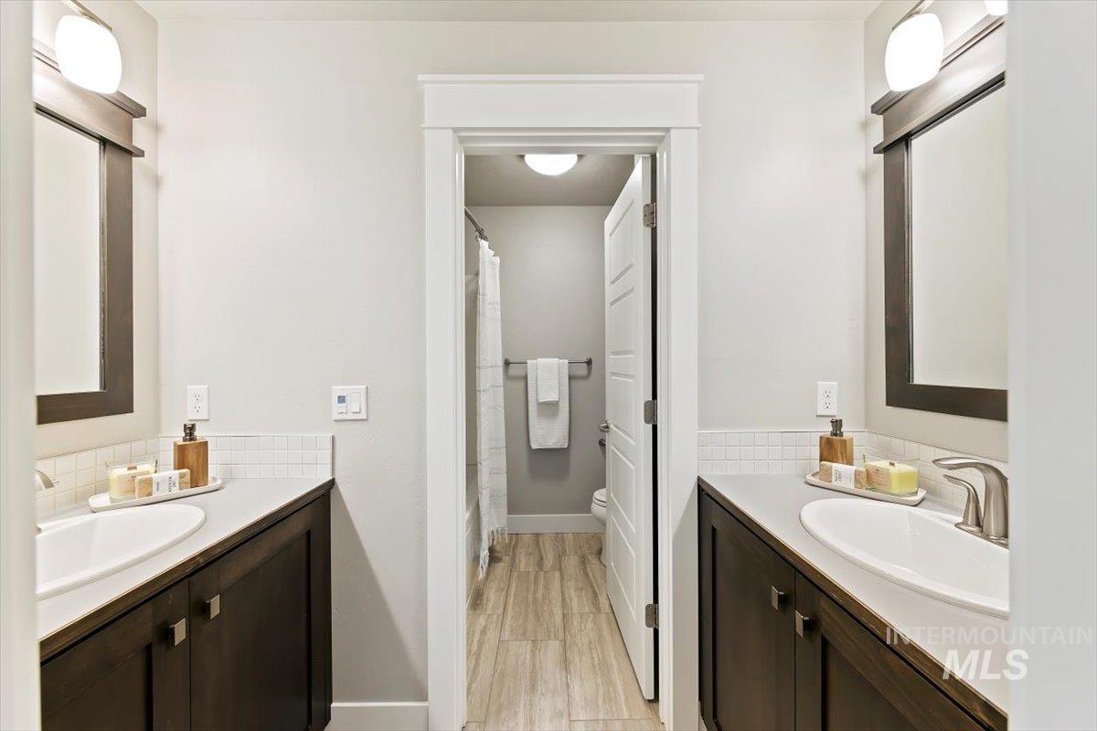 Bathroom with two vanities, light wood-style floors, and shower / bathtub combination with curtain