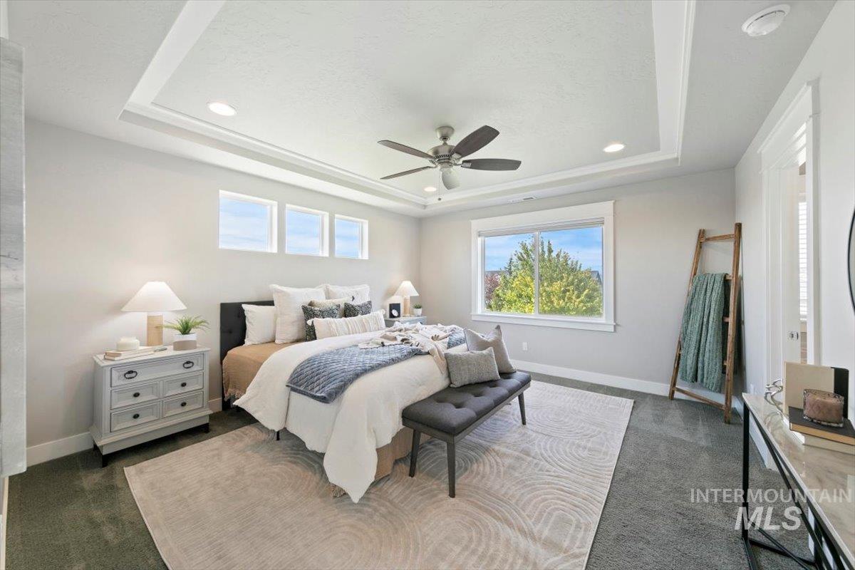 Bedroom with a tray ceiling, dark colored carpet, multiple windows, and recessed lighting