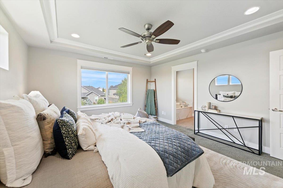 Bedroom featuring a raised ceiling, carpet flooring, ensuite bath, ceiling fan, and recessed lighting