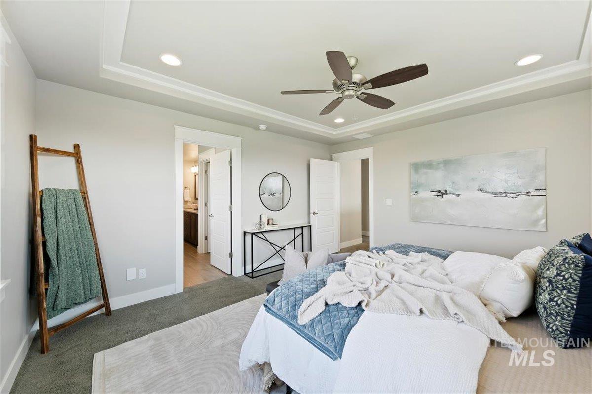 Bedroom with a raised ceiling, carpet flooring, ceiling fan, recessed lighting, and ensuite bath