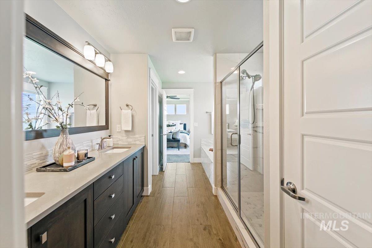 Ensuite bathroom with a stall shower, double vanity, light wood finished floors, and recessed lighting