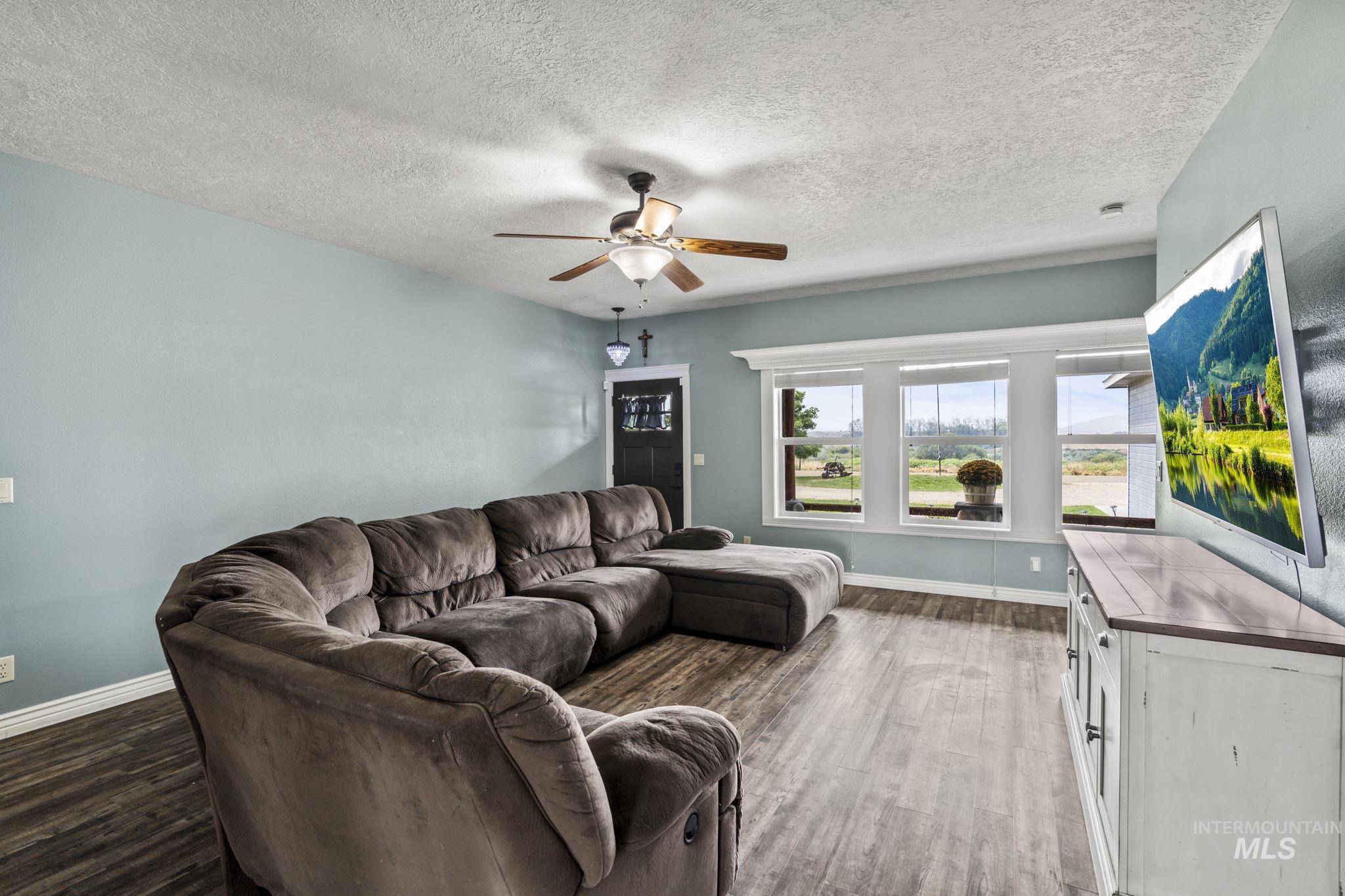 Living room with a ceiling fan, a textured ceiling, and wood finished floors