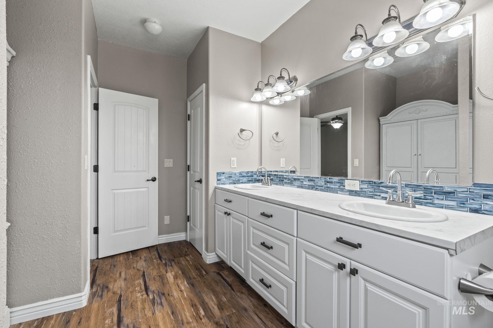 Full bathroom with double vanity, dark wood-type flooring, decorative backsplash, a textured wall, and a ceiling fan