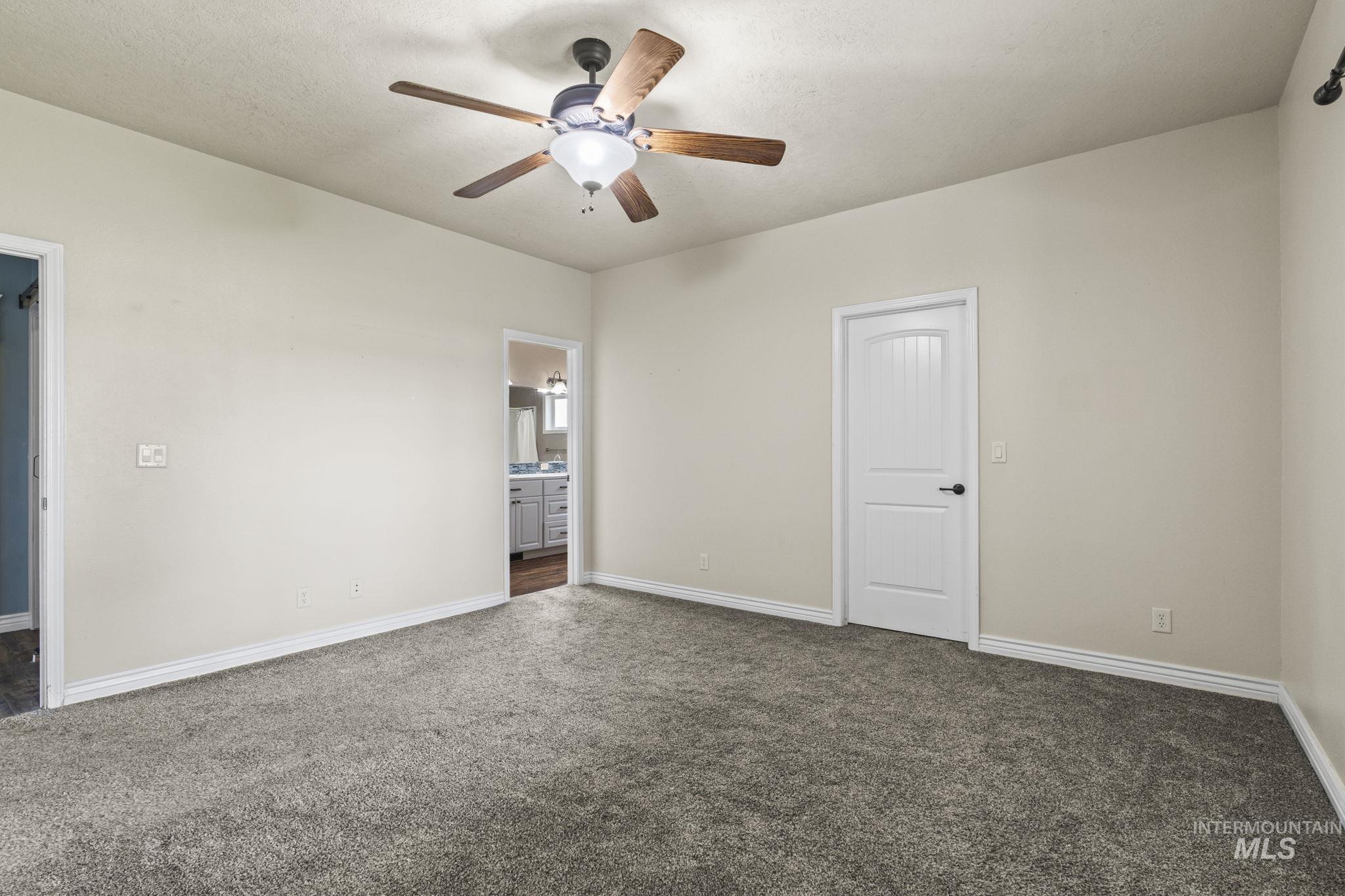 Unfurnished bedroom featuring dark carpet, a ceiling fan, connected bathroom, and a textured ceiling