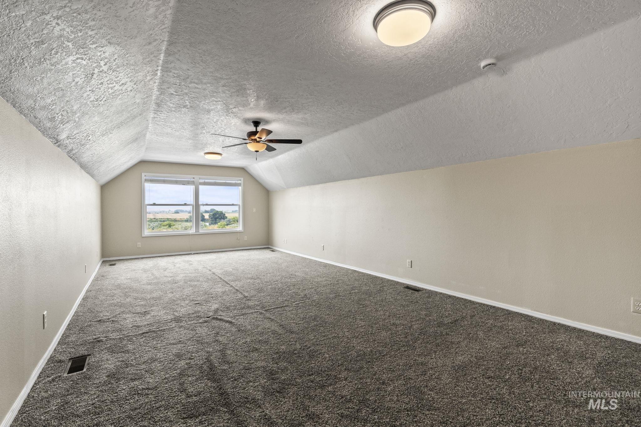 Additional living space with carpet, lofted ceiling, a textured ceiling, and a ceiling fan