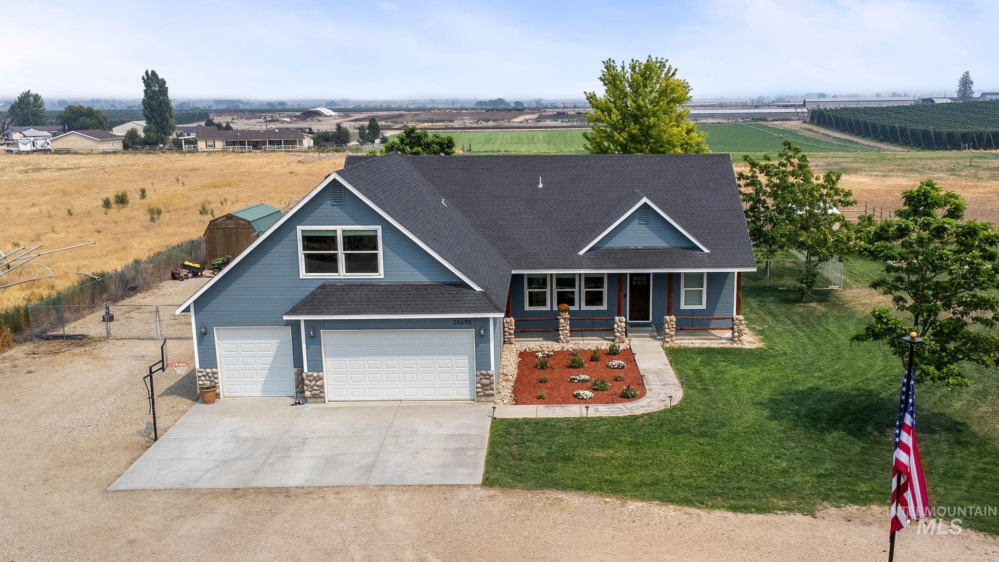 View of front of property with concrete driveway, covered porch, roof with shingles, stone siding, and a view of rural / pastoral area
