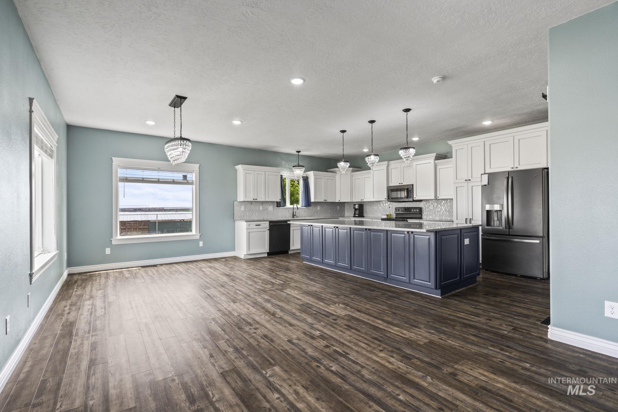 Kitchen featuring appliances with stainless steel finishes, white cabinets, a kitchen island, decorative light fixtures, and dark wood-type flooring