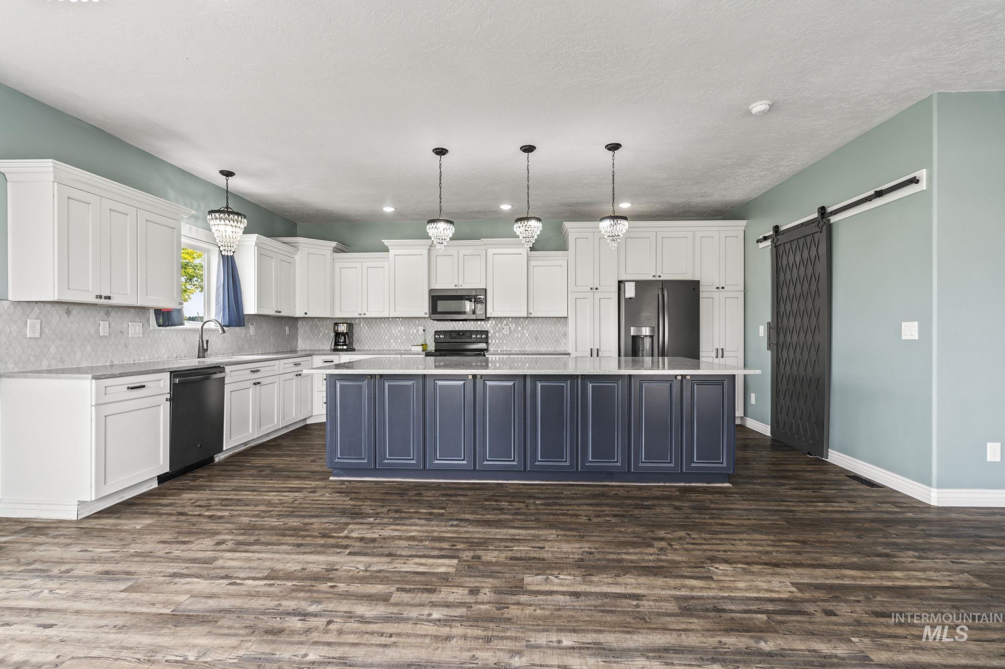 Kitchen with a barn door, white cabinetry, stainless steel appliances, dark wood-type flooring, and decorative backsplash