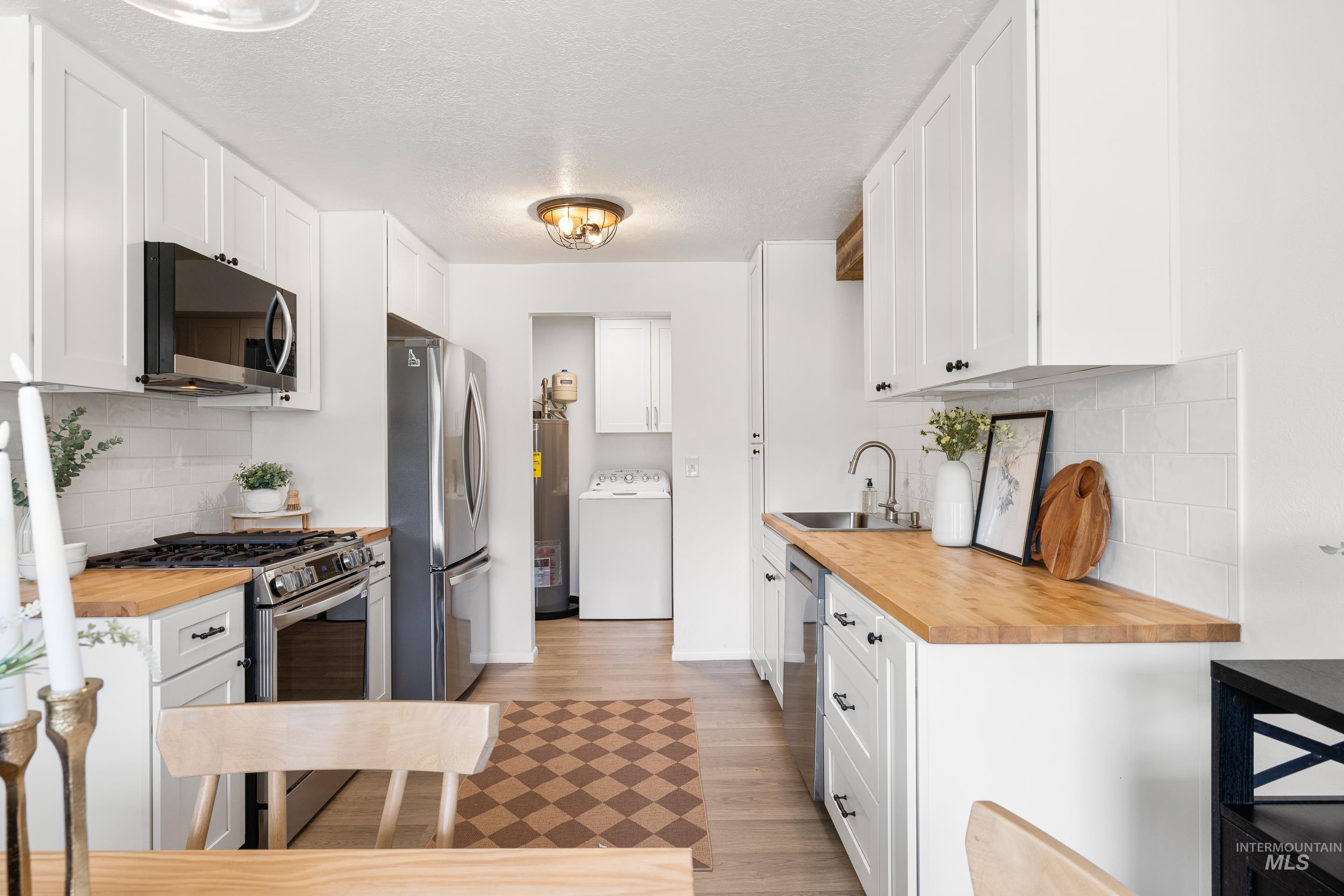 Kitchen with backsplash, butcher block countertops, white cabinets, appliances with stainless steel finishes, and a textured ceiling