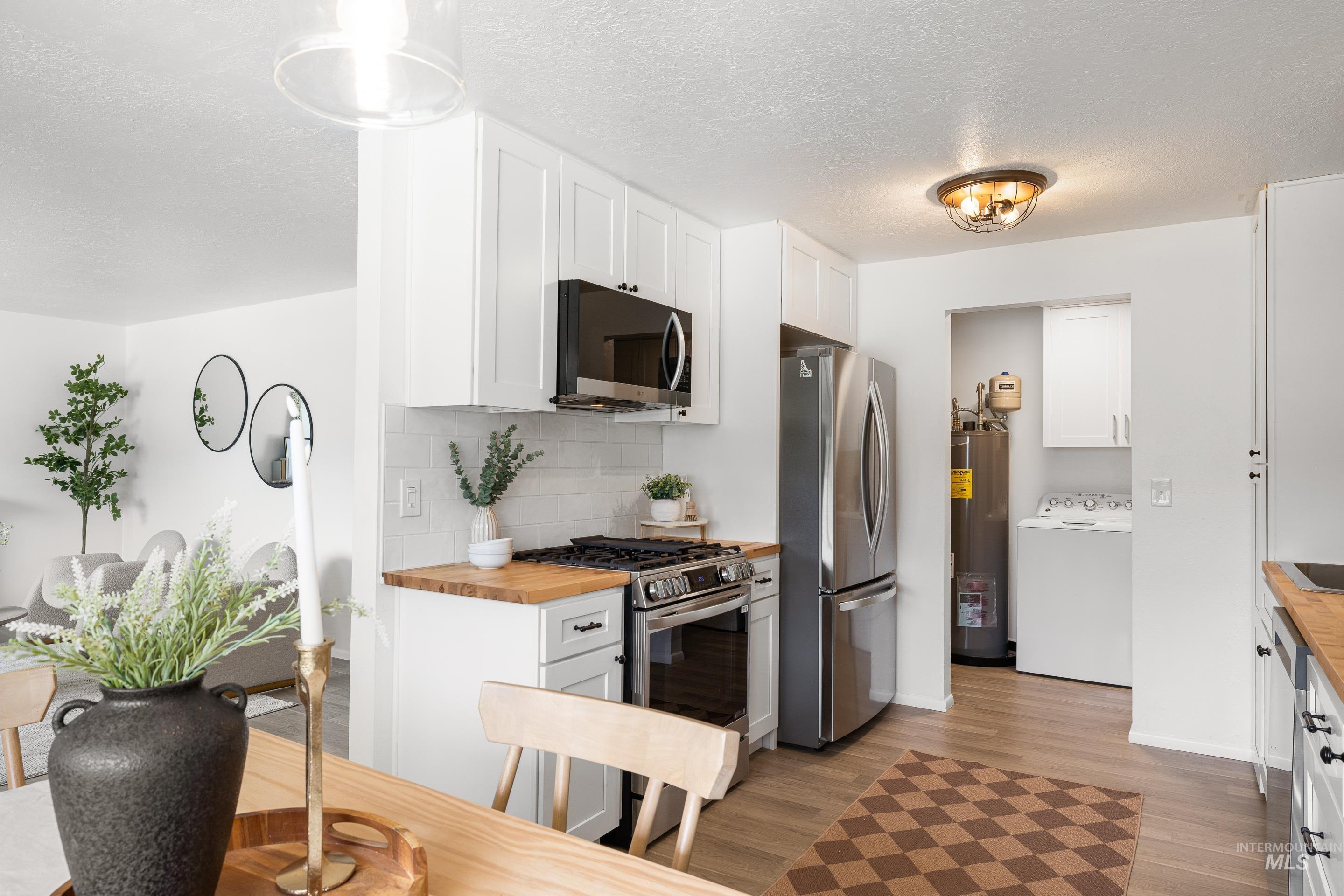 Kitchen with wooden counters, white cabinetry, stainless steel appliances, tasteful backsplash, and a textured ceiling