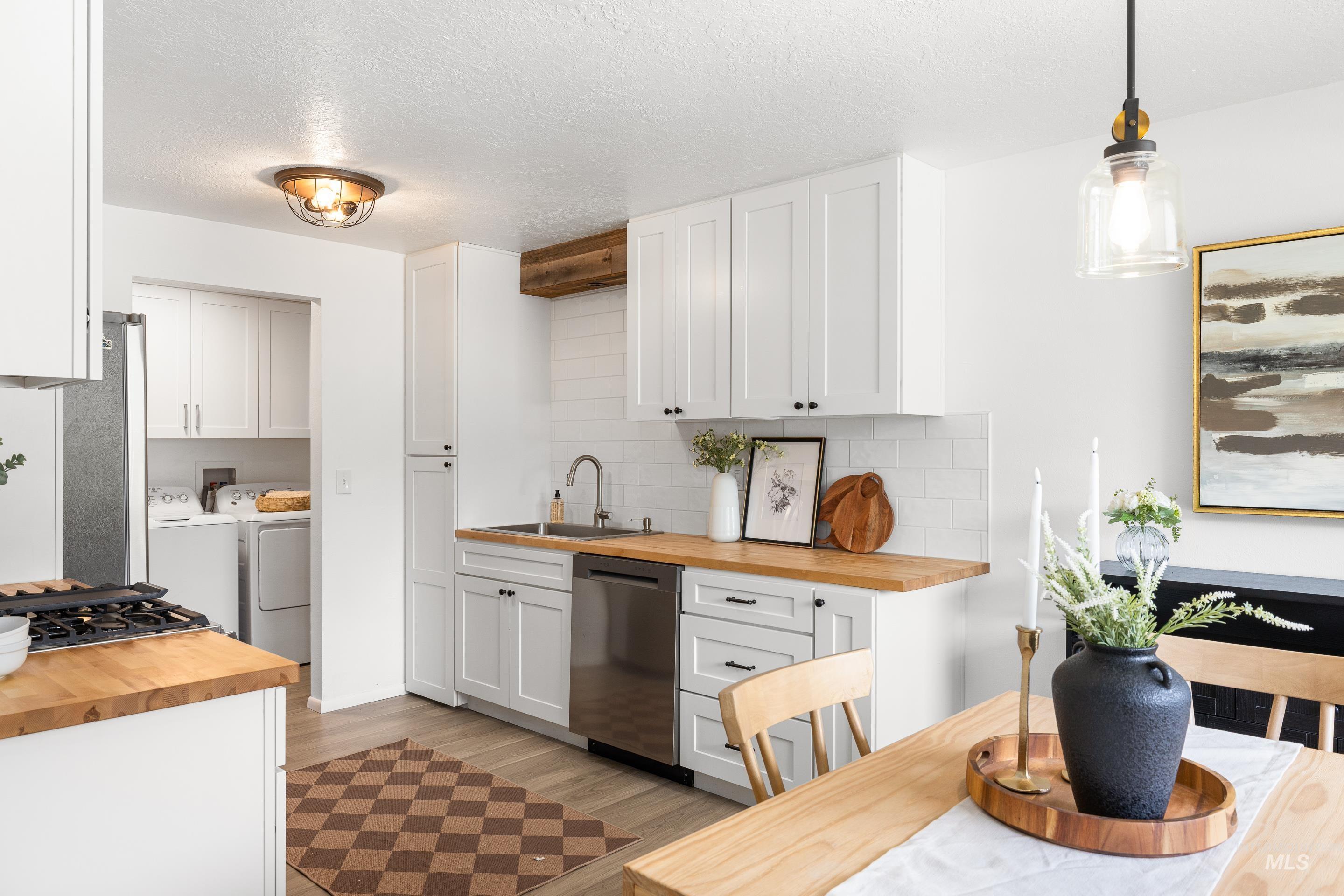 Kitchen featuring butcher block counters, white cabinets, a textured ceiling, stainless steel appliances, and washing machine and clothes dryer