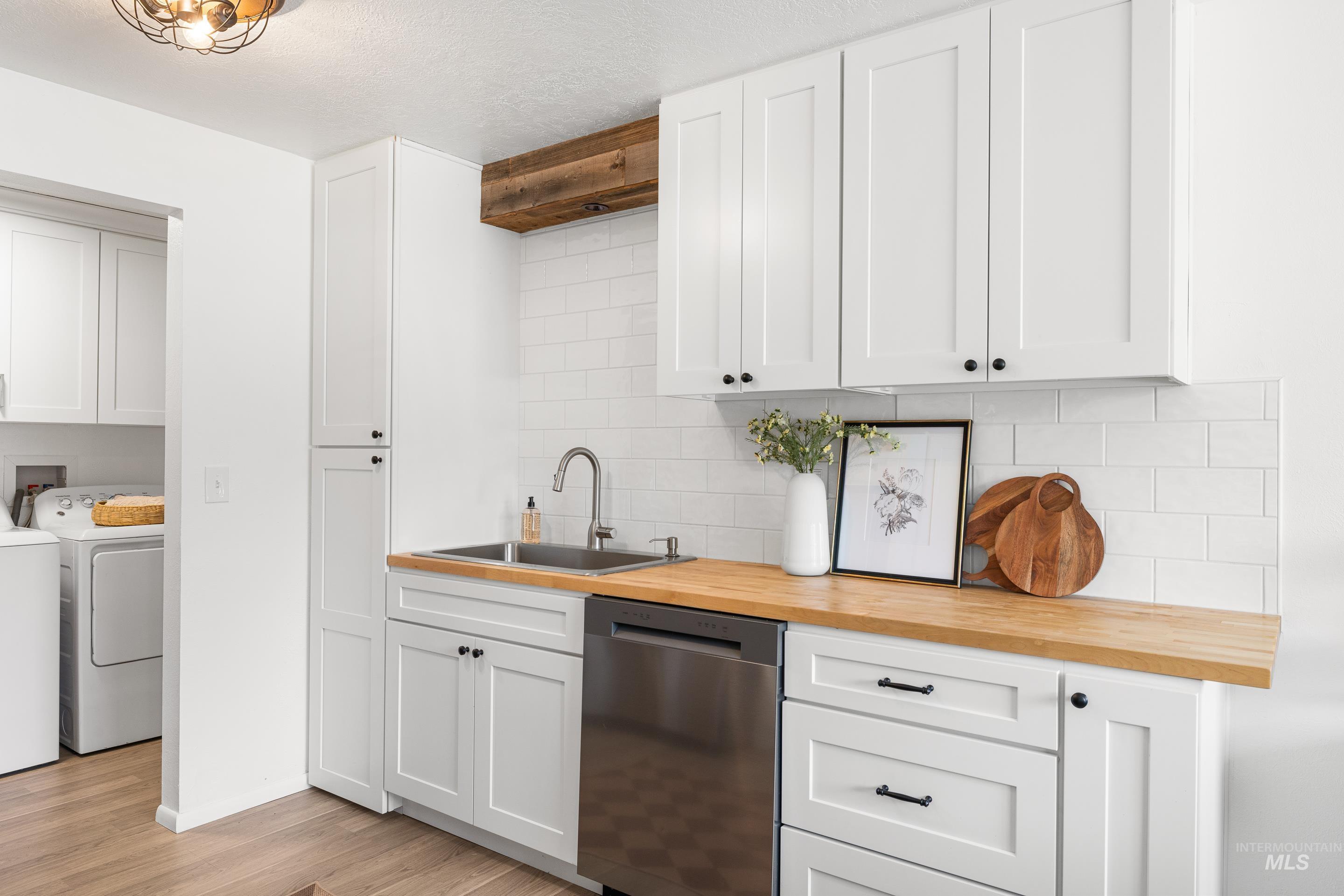 Kitchen featuring tasteful backsplash, butcher block countertops, white cabinetry, stainless steel dishwasher, and light wood-type flooring