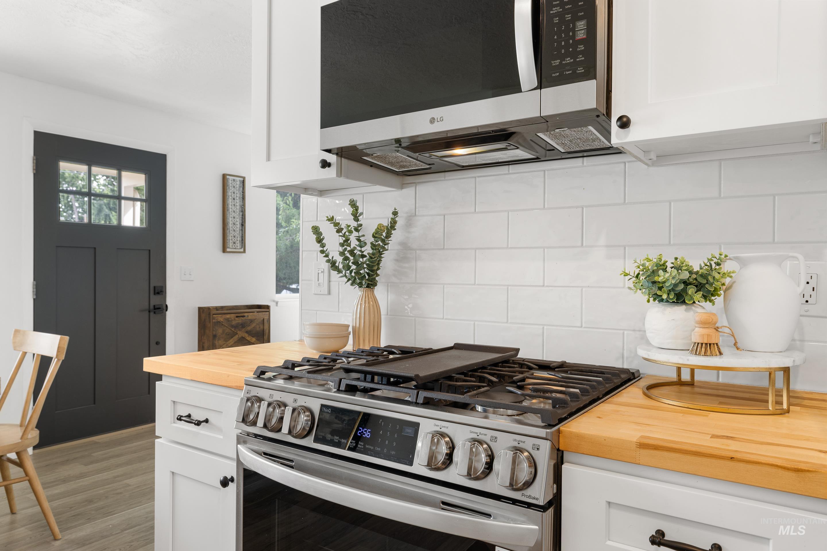 Kitchen featuring white cabinets, butcher block countertops, appliances with stainless steel finishes, and backsplash