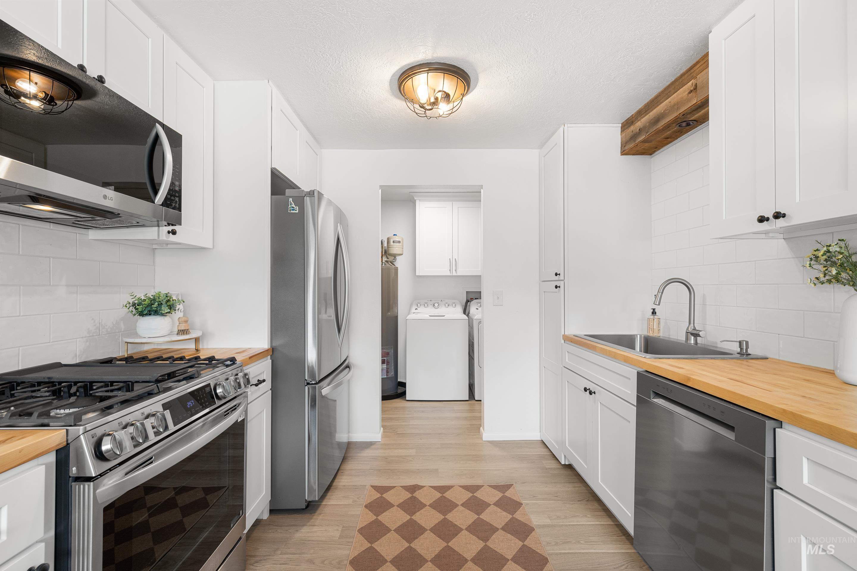 Kitchen with butcher block counters, tasteful backsplash, stainless steel appliances, light wood-type flooring, and a textured ceiling