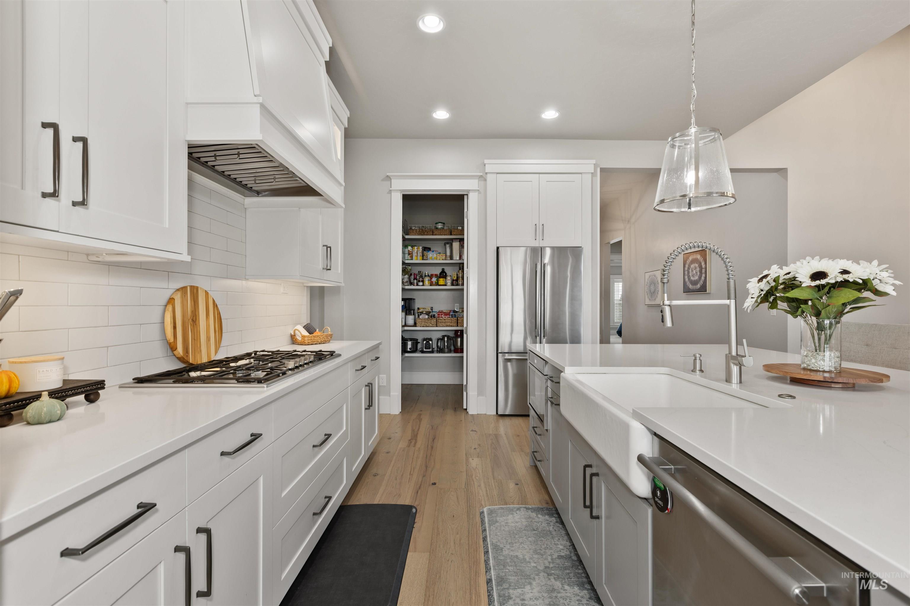 Kitchen featuring white cabinets, recessed lighting, light wood-style floors, appliances with stainless steel finishes, and hanging light fixtures