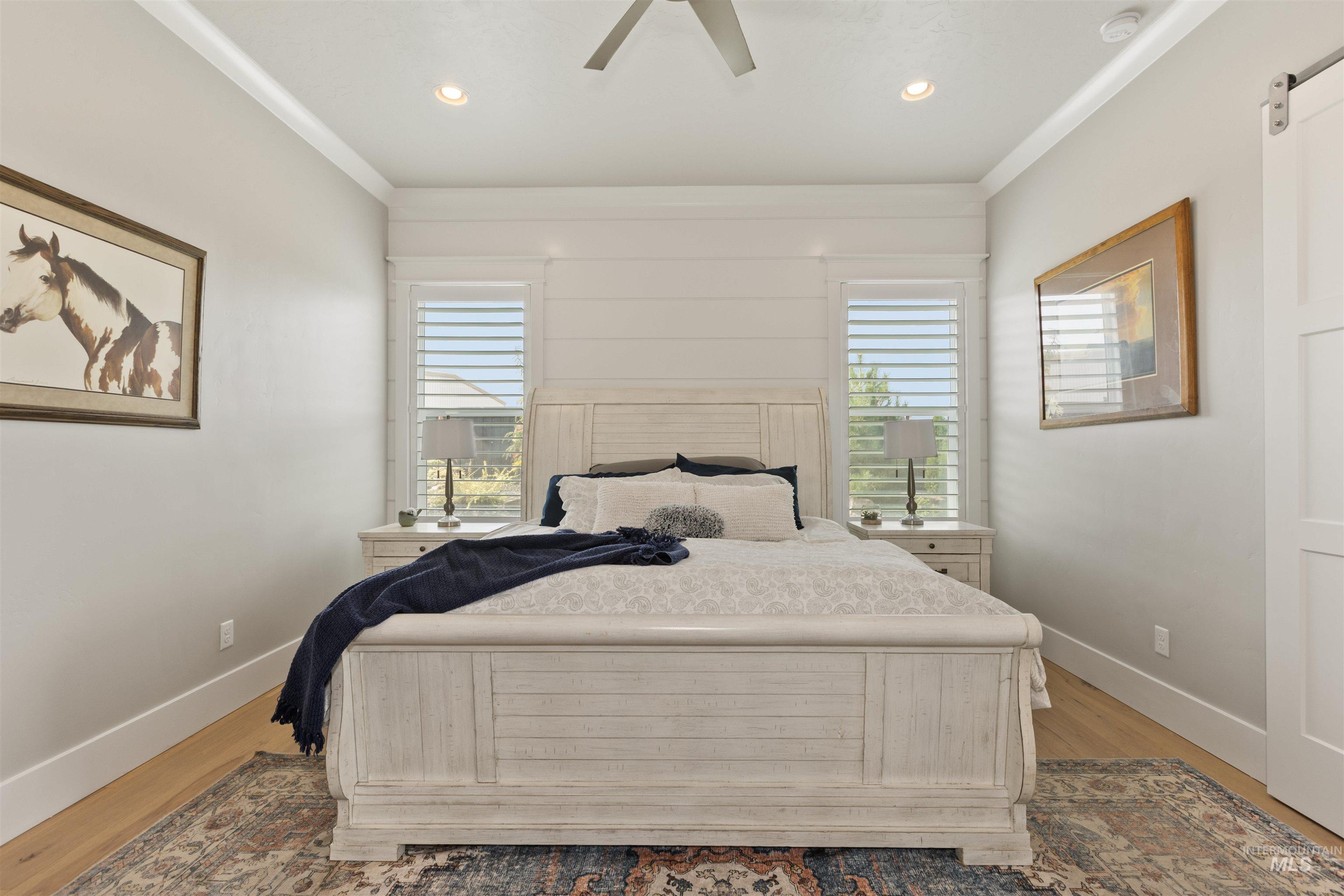 Bedroom with wood finished floors, crown molding, a ceiling fan, recessed lighting, and a barn door