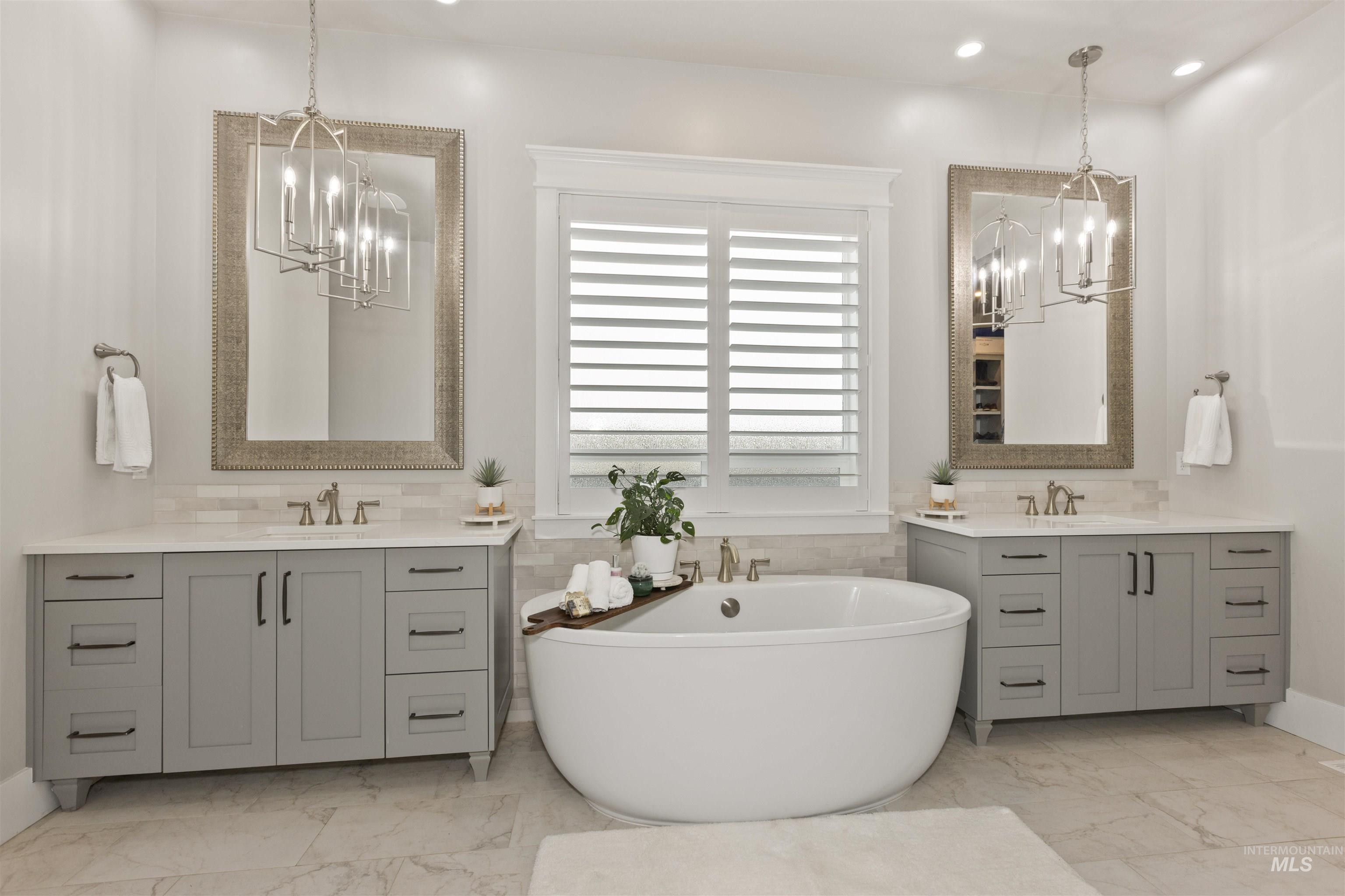 Bathroom featuring a chandelier, light marble finish floors, a freestanding tub, two vanities, and recessed lighting
