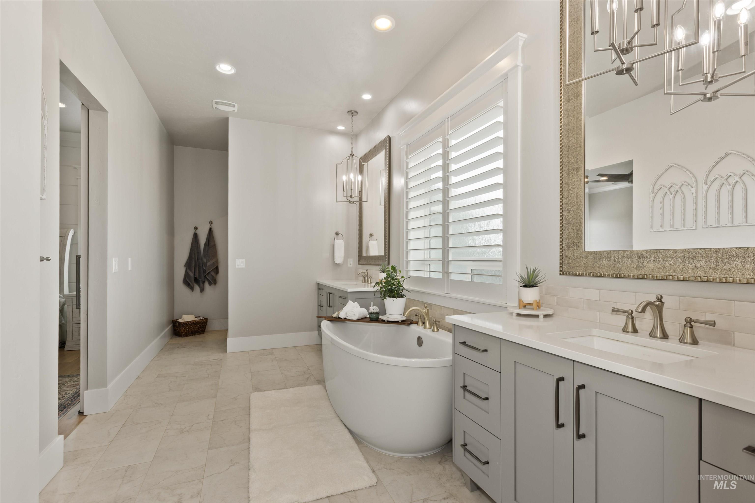 Full bathroom featuring a chandelier, recessed lighting, a freestanding tub, two vanities, and decorative backsplash