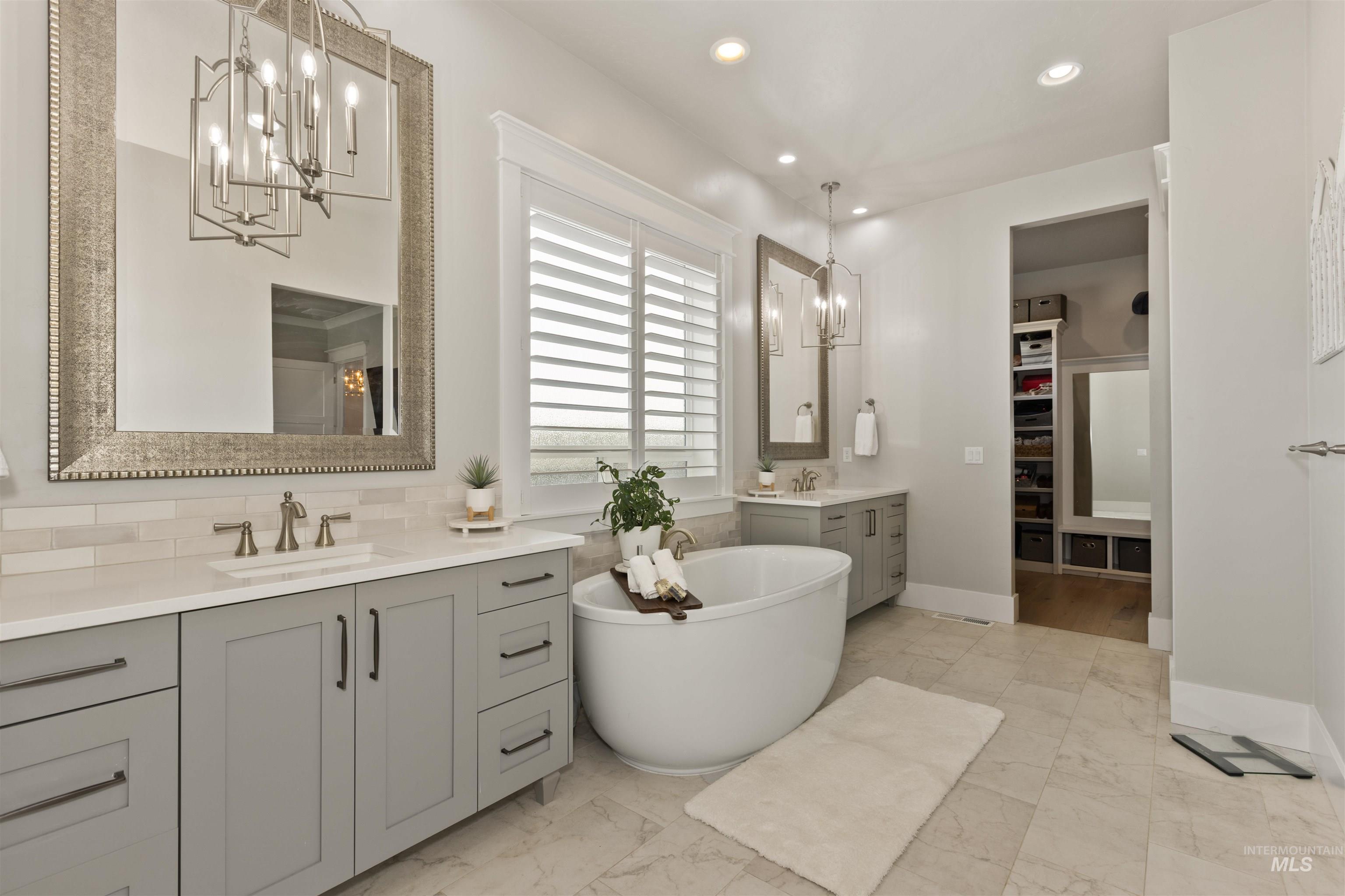Full bath with a chandelier, light marble finish flooring, two vanities, a spacious closet, and a freestanding tub