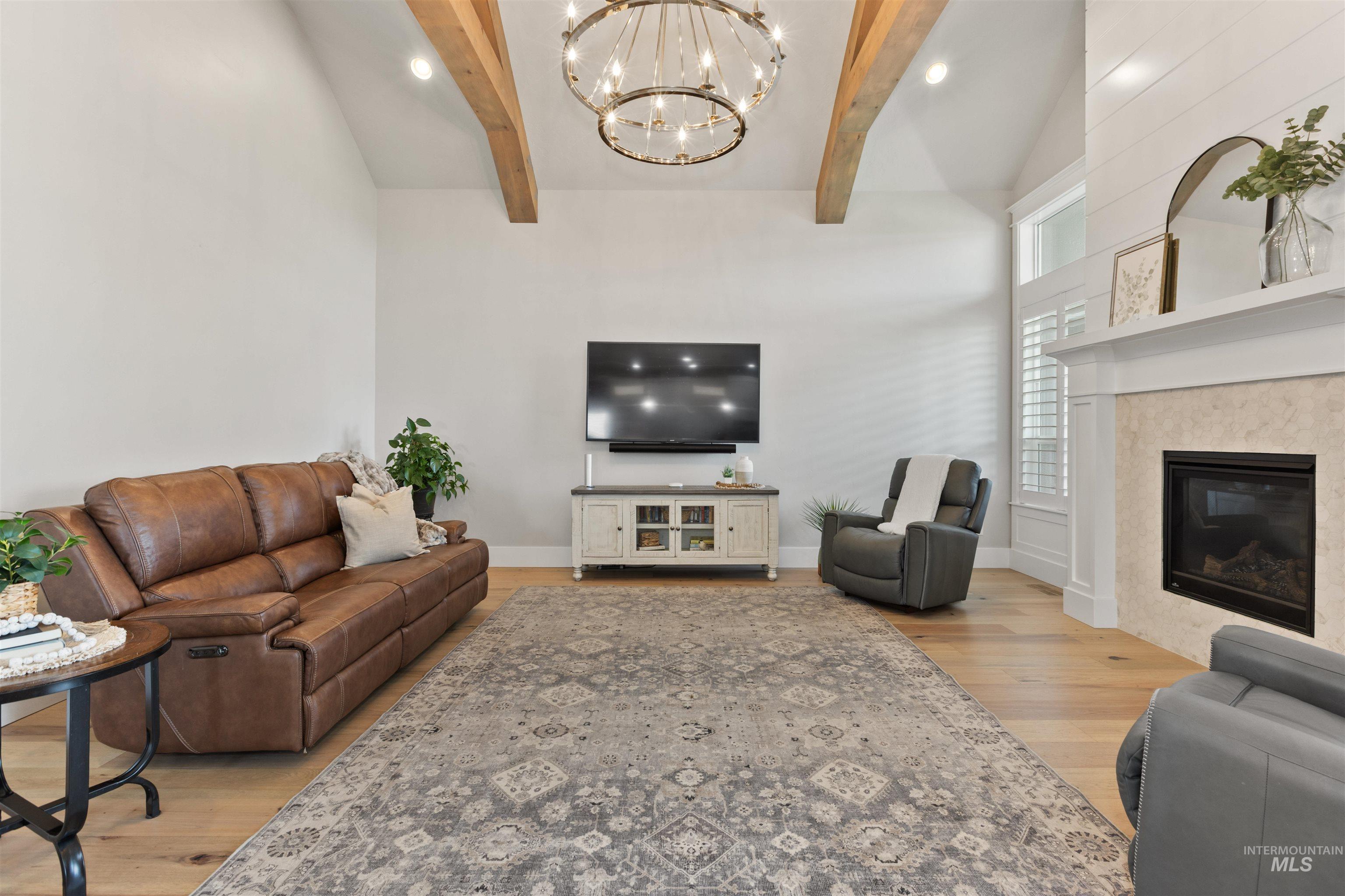 Living area featuring light wood-type flooring, a fireplace, beam ceiling, a chandelier, and recessed lighting