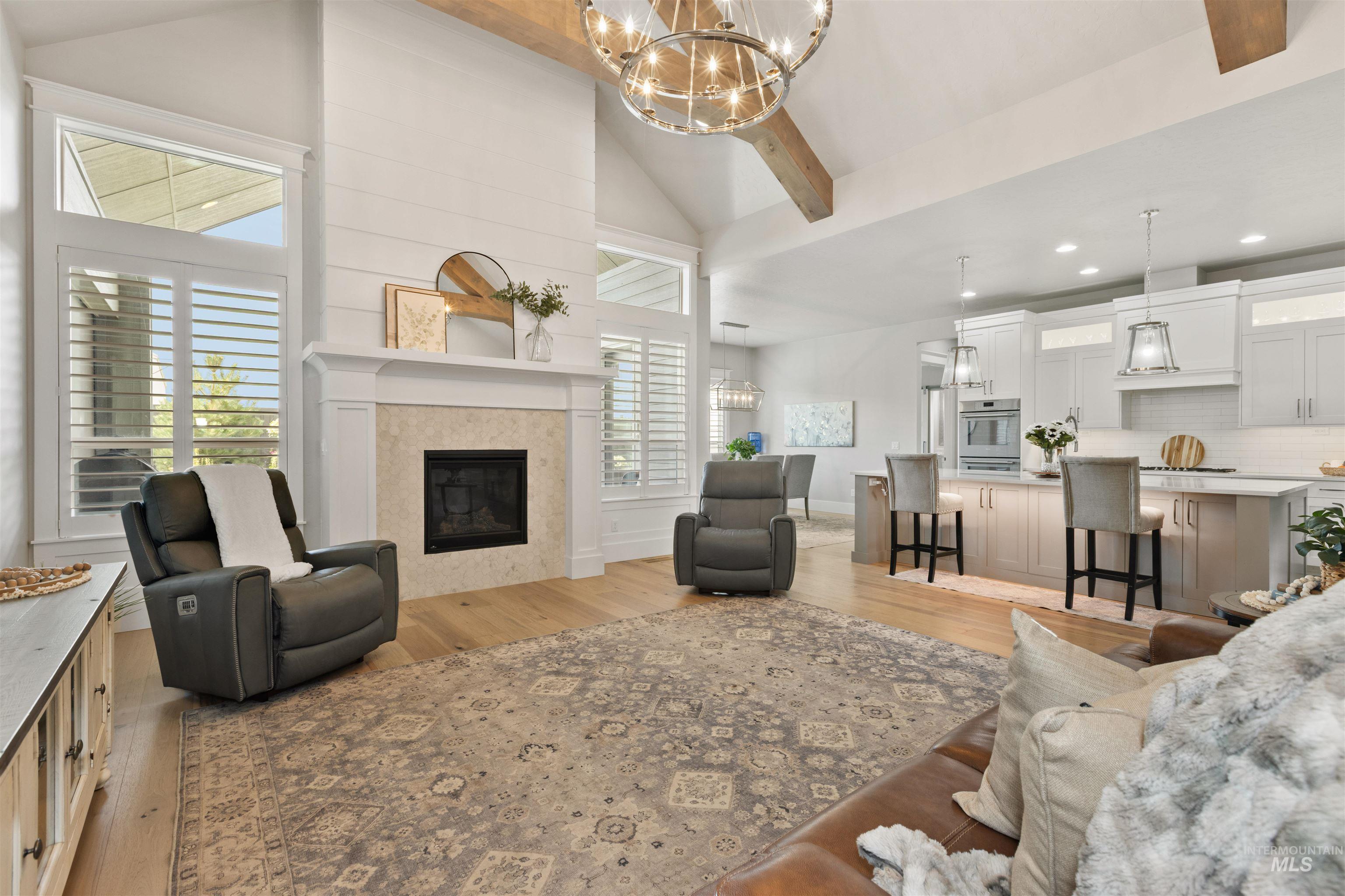 Living room with light wood-style floors, high vaulted ceiling, beam ceiling, a chandelier, and a tiled fireplace