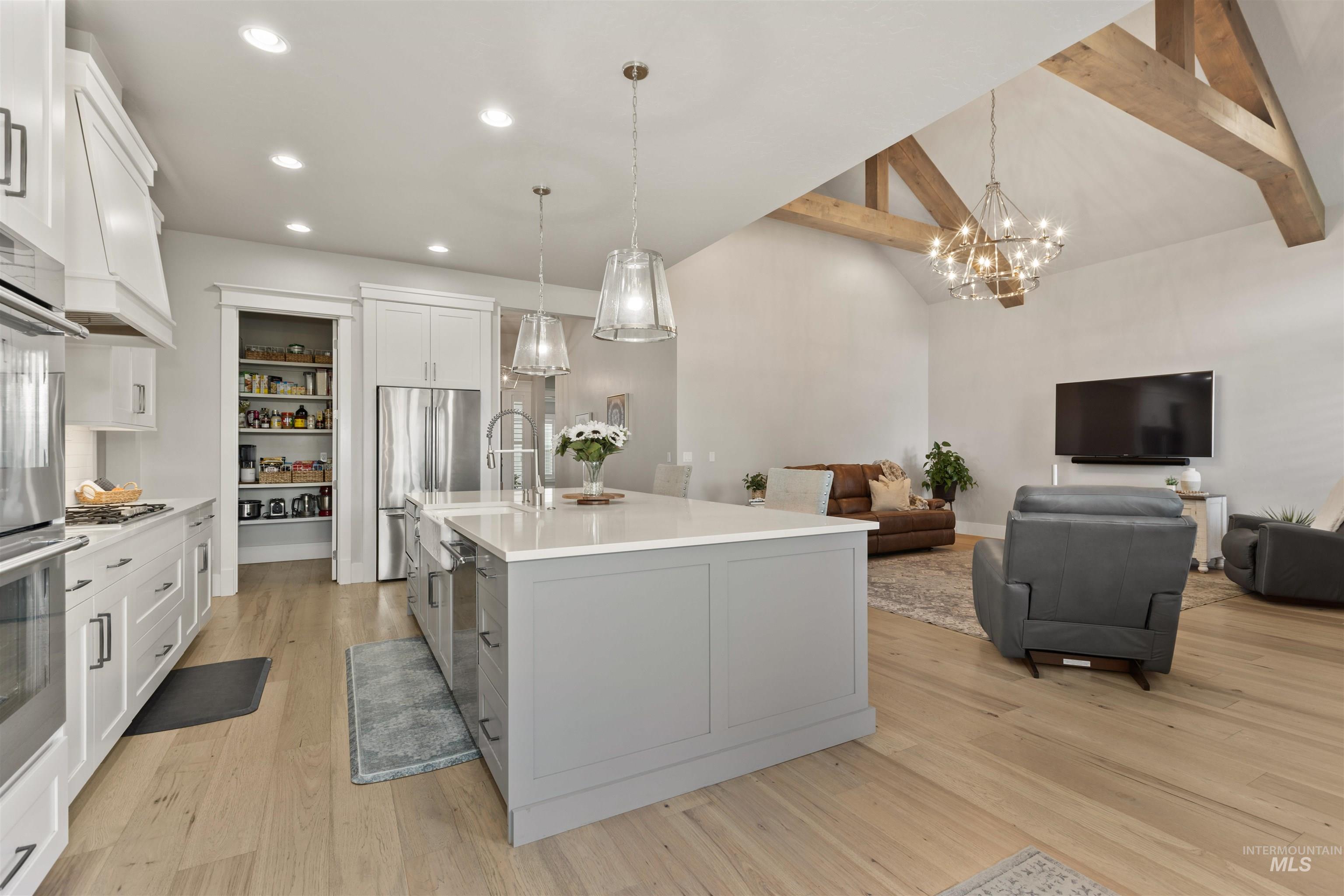 Kitchen with white cabinets, pendant lighting, a kitchen island with sink, open floor plan, and light wood-type flooring