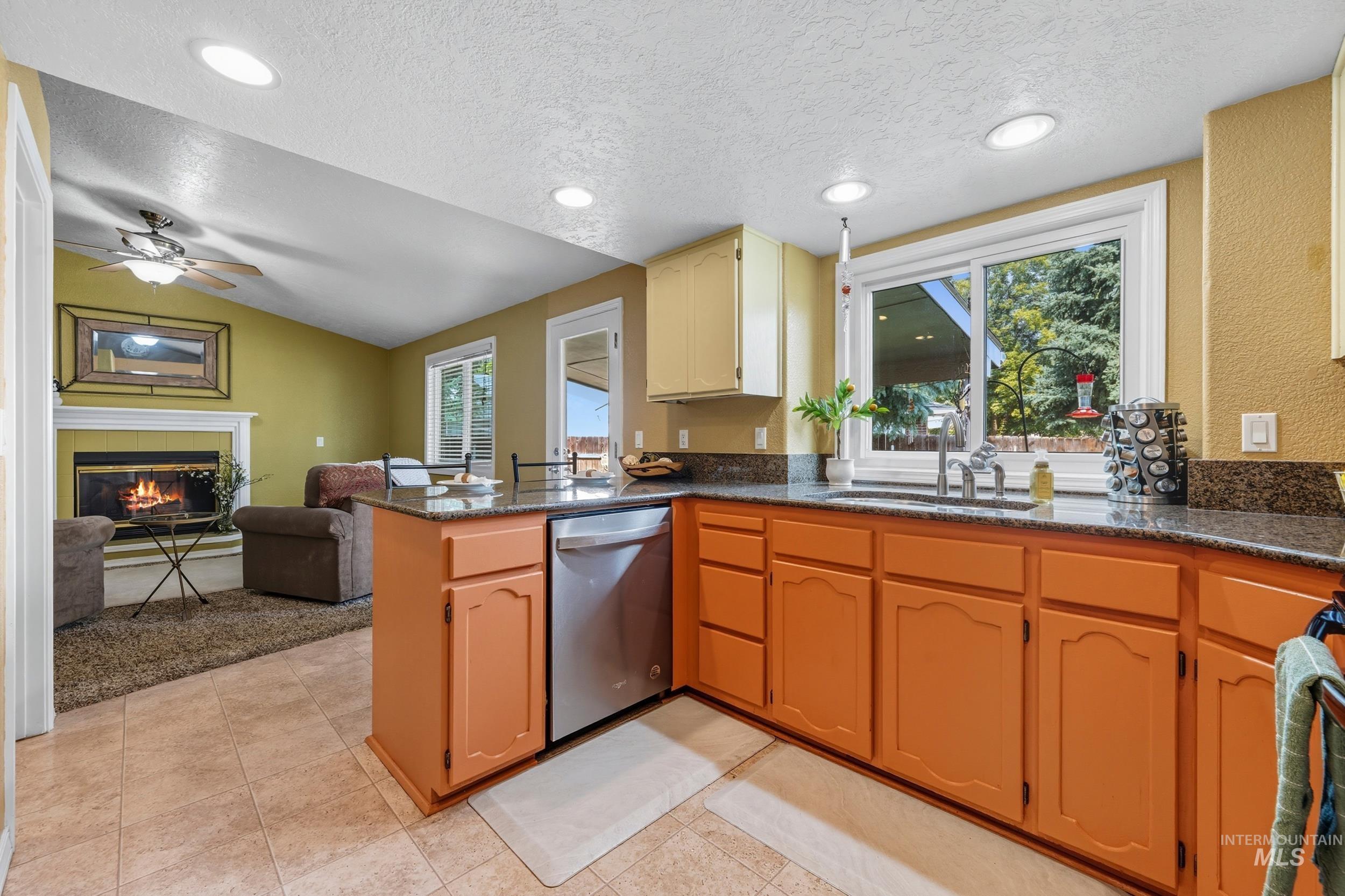 Kitchen with a peninsula, a tile fireplace, a textured ceiling, open floor plan, and dishwasher