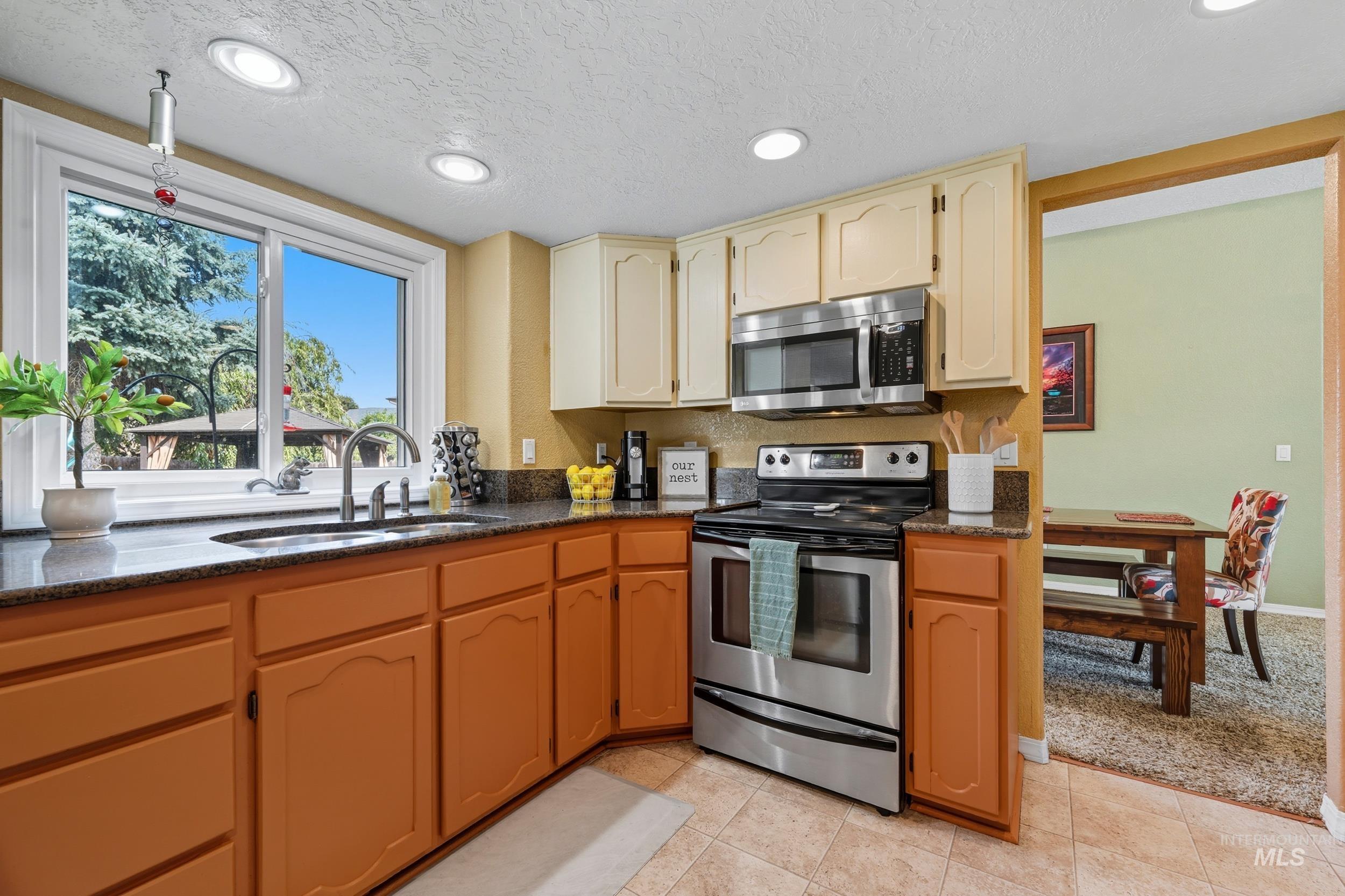 Kitchen with stainless steel appliances, a textured ceiling, recessed lighting, dark stone counters, and light tile patterned floors