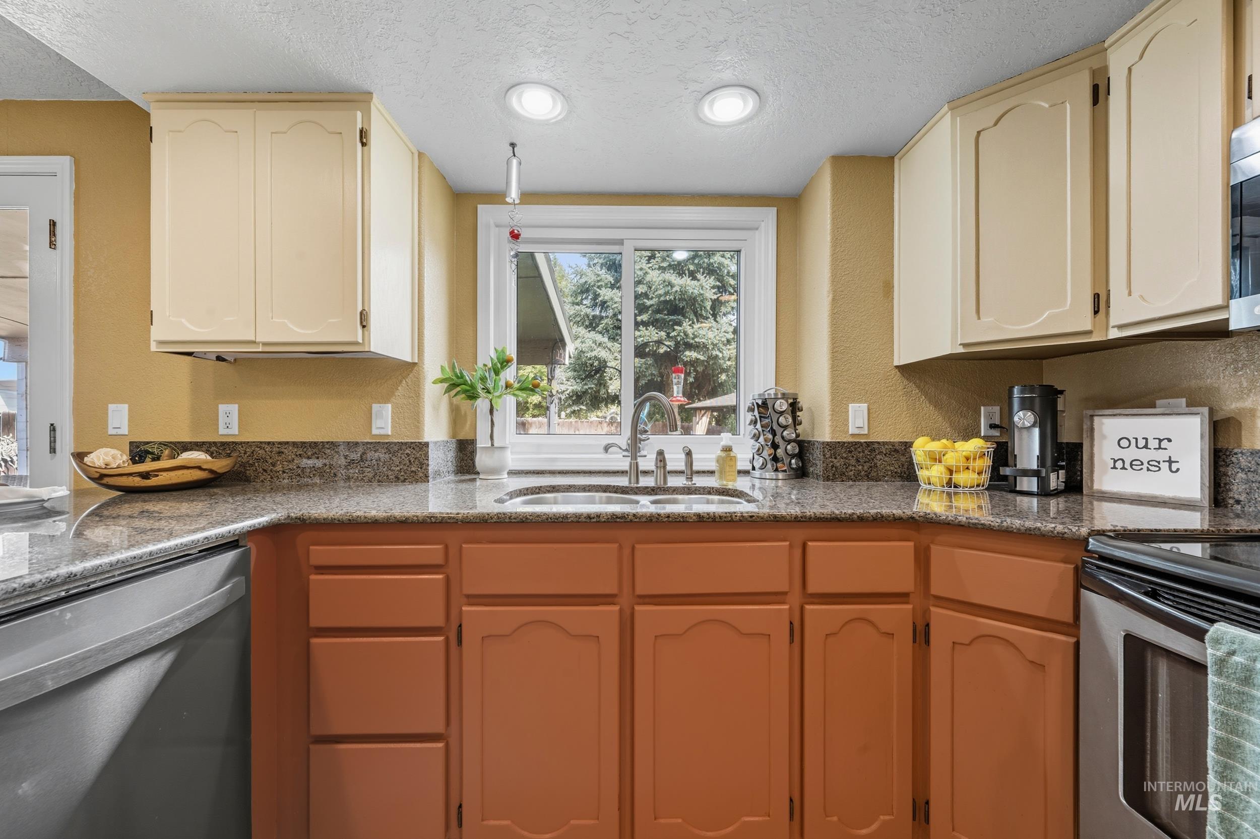 Kitchen with stainless steel appliances, a textured ceiling, a textured wall, recessed lighting, and dark stone counters