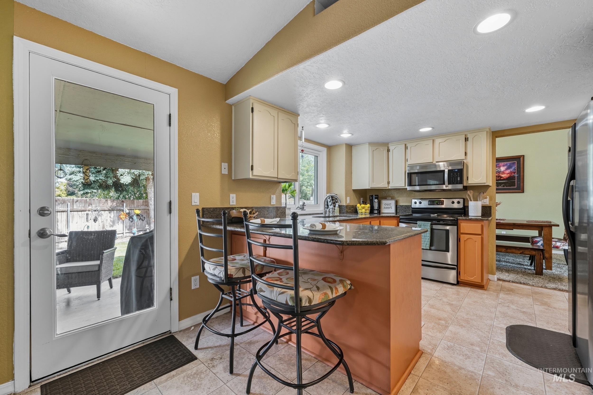Kitchen featuring a peninsula, a kitchen bar, appliances with stainless steel finishes, recessed lighting, and dark stone countertops