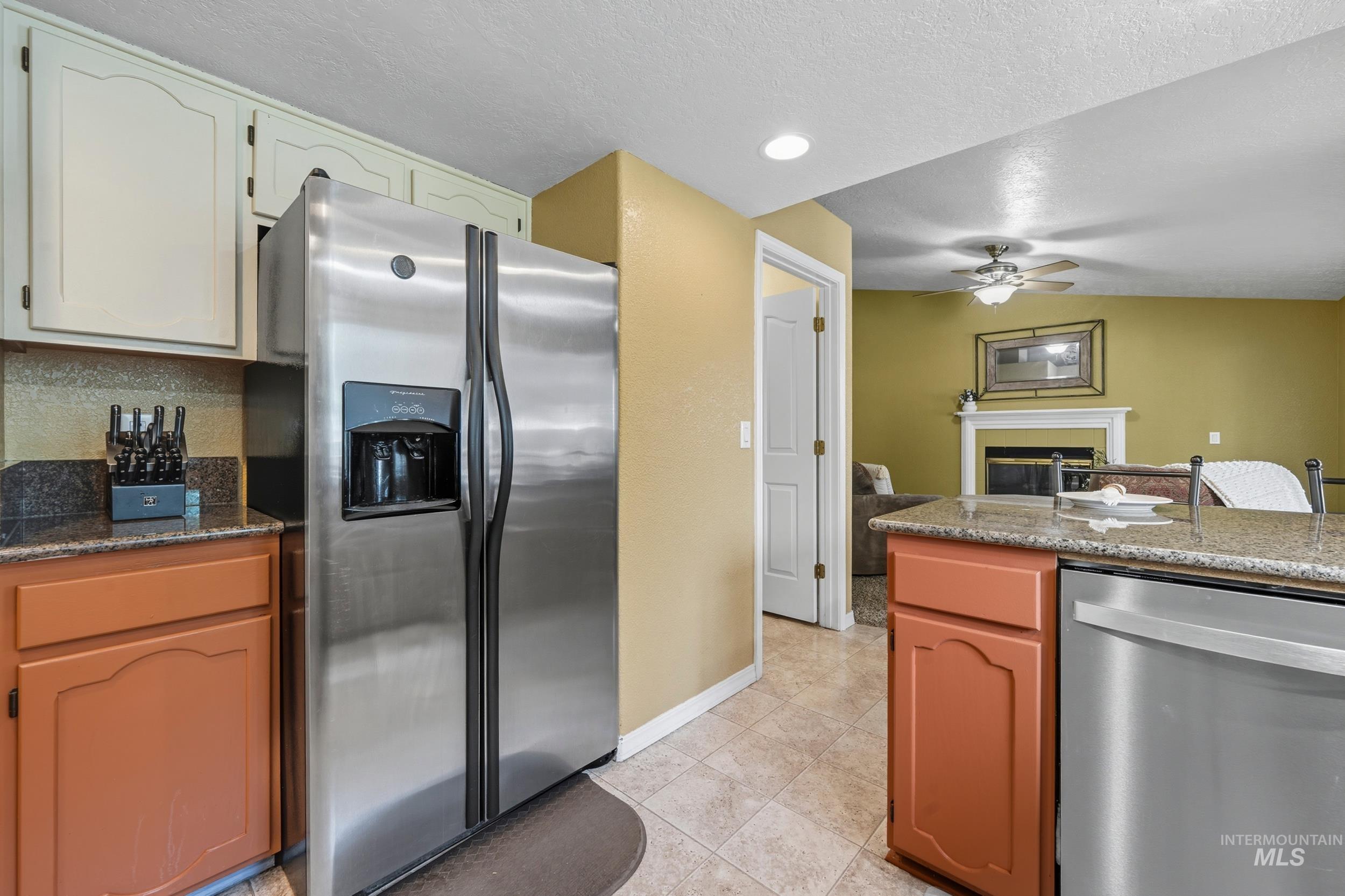 Kitchen featuring appliances with stainless steel finishes, a fireplace, dark stone counters, a textured ceiling, and a ceiling fan