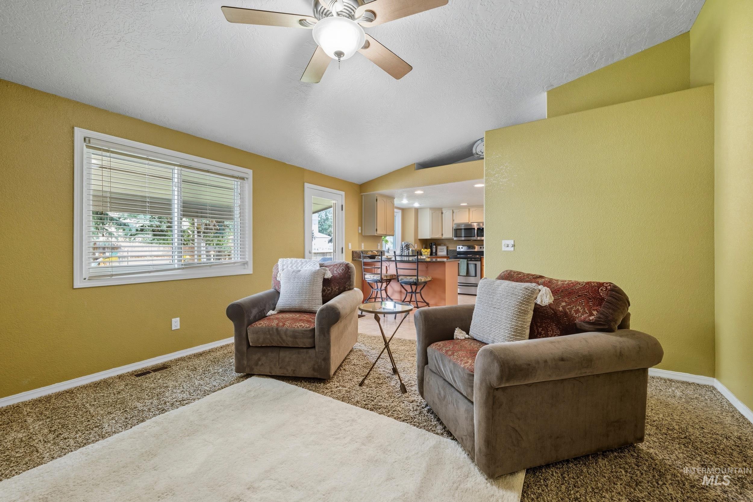 Carpeted living room featuring lofted ceiling, a textured ceiling, and a ceiling fan