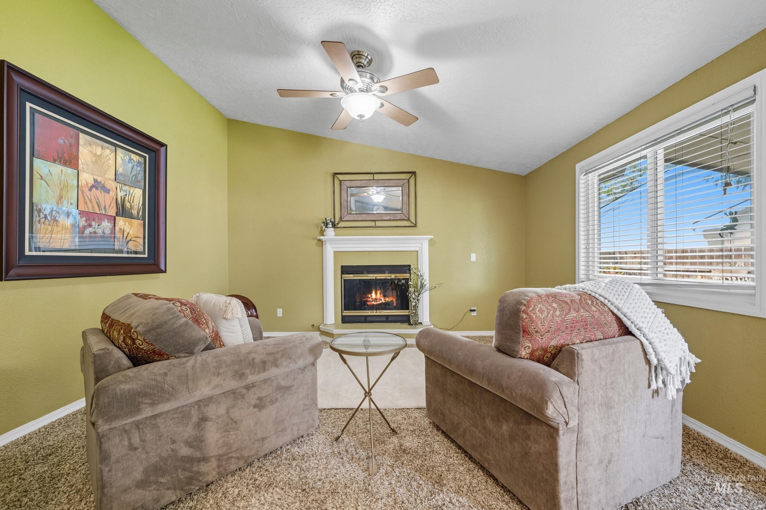 Carpeted living room featuring a glass covered fireplace, lofted ceiling, and ceiling fan