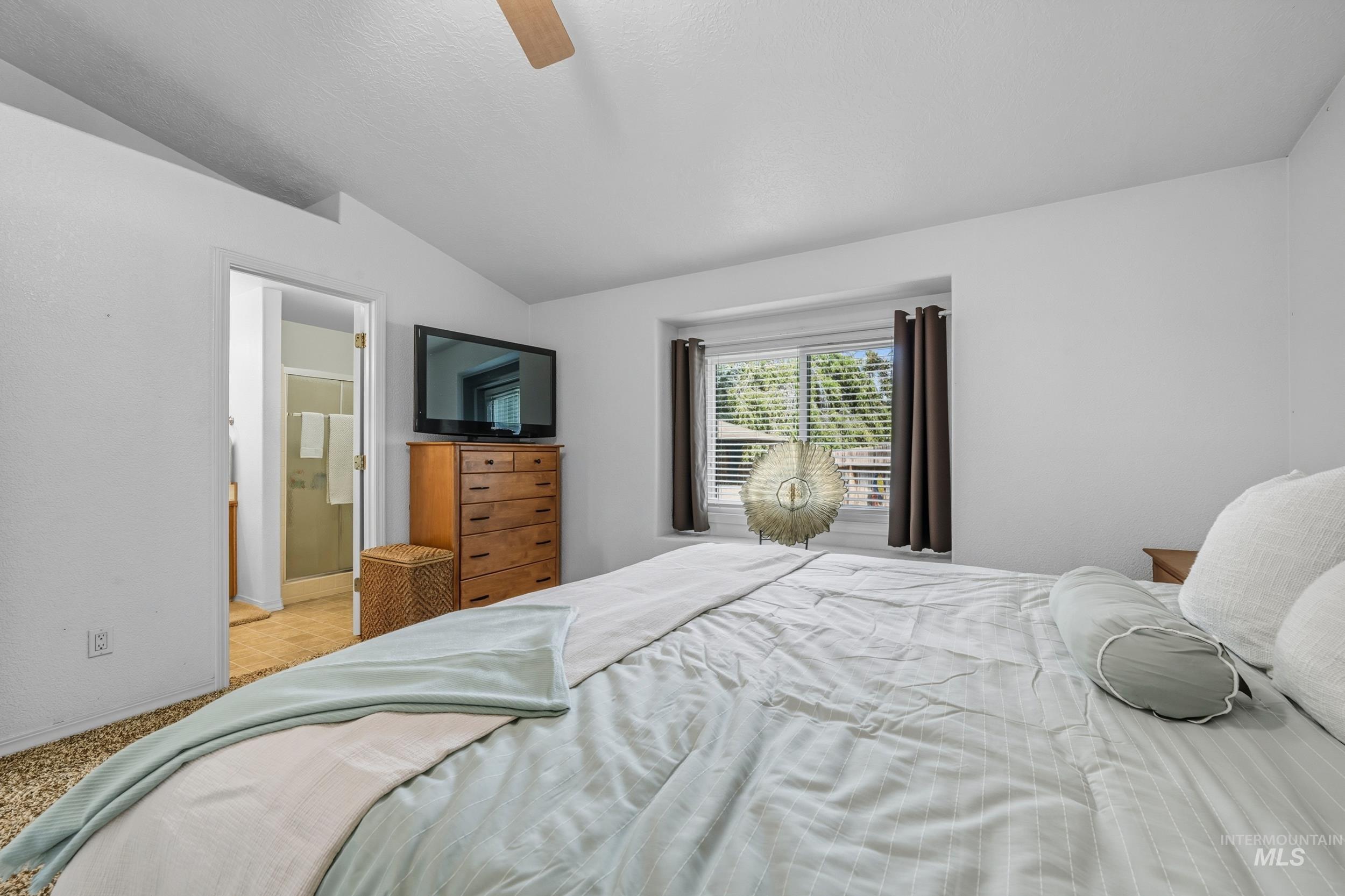 Bedroom with lofted ceiling, ceiling fan, carpet floors, and connected bathroom