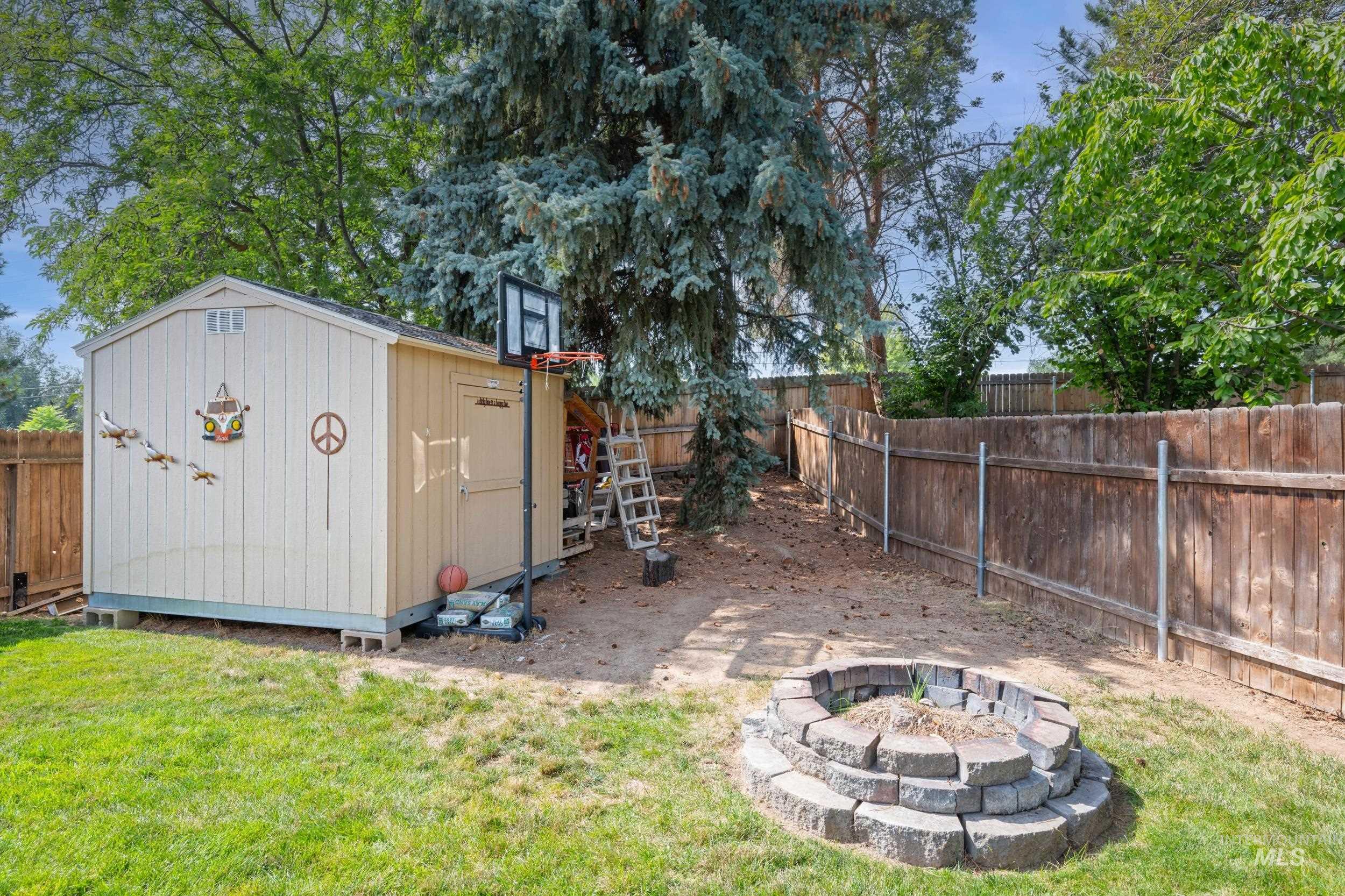 Fenced backyard featuring a fire pit, a shed, and a patio area