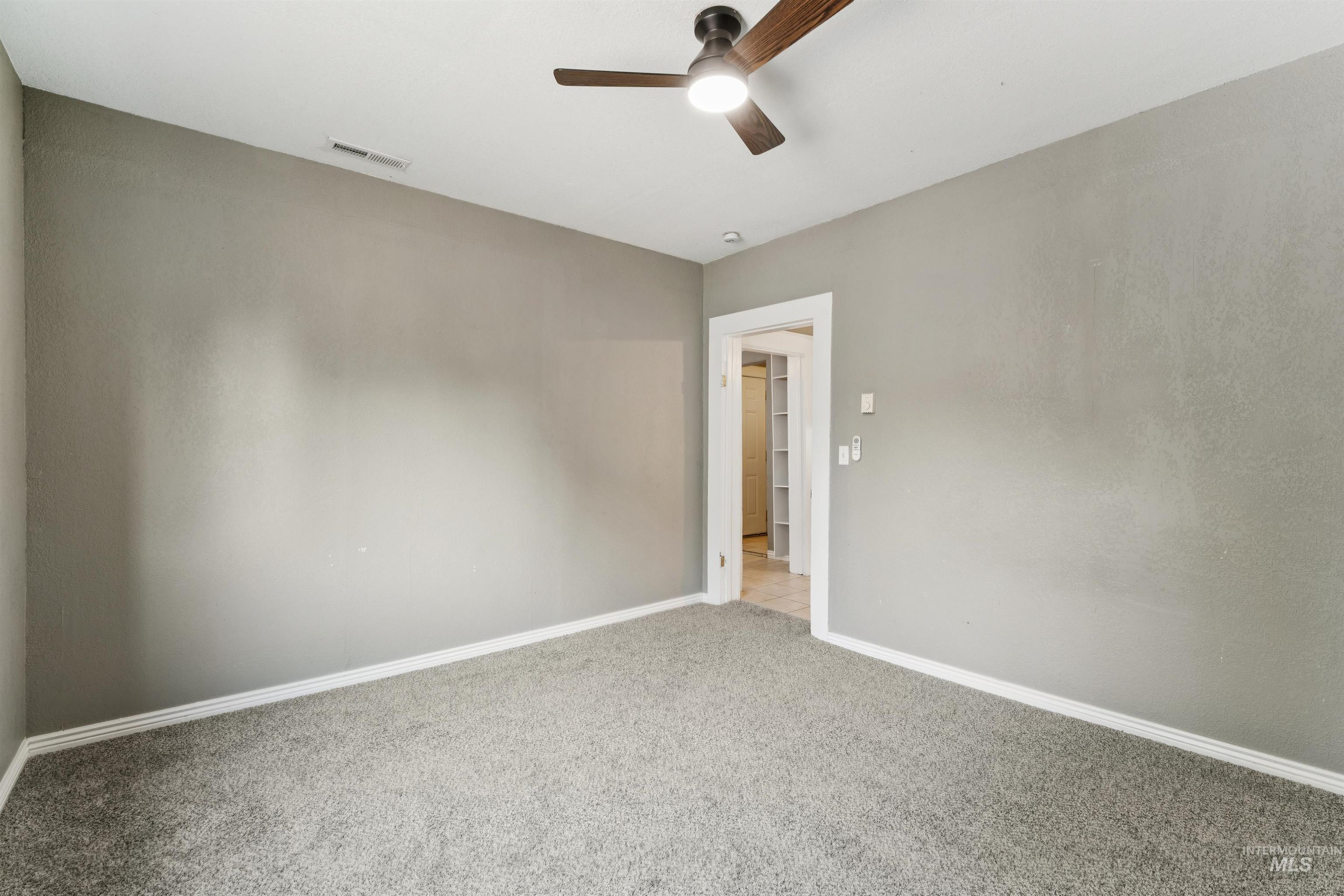 Carpeted empty room with baseboards and a ceiling fan